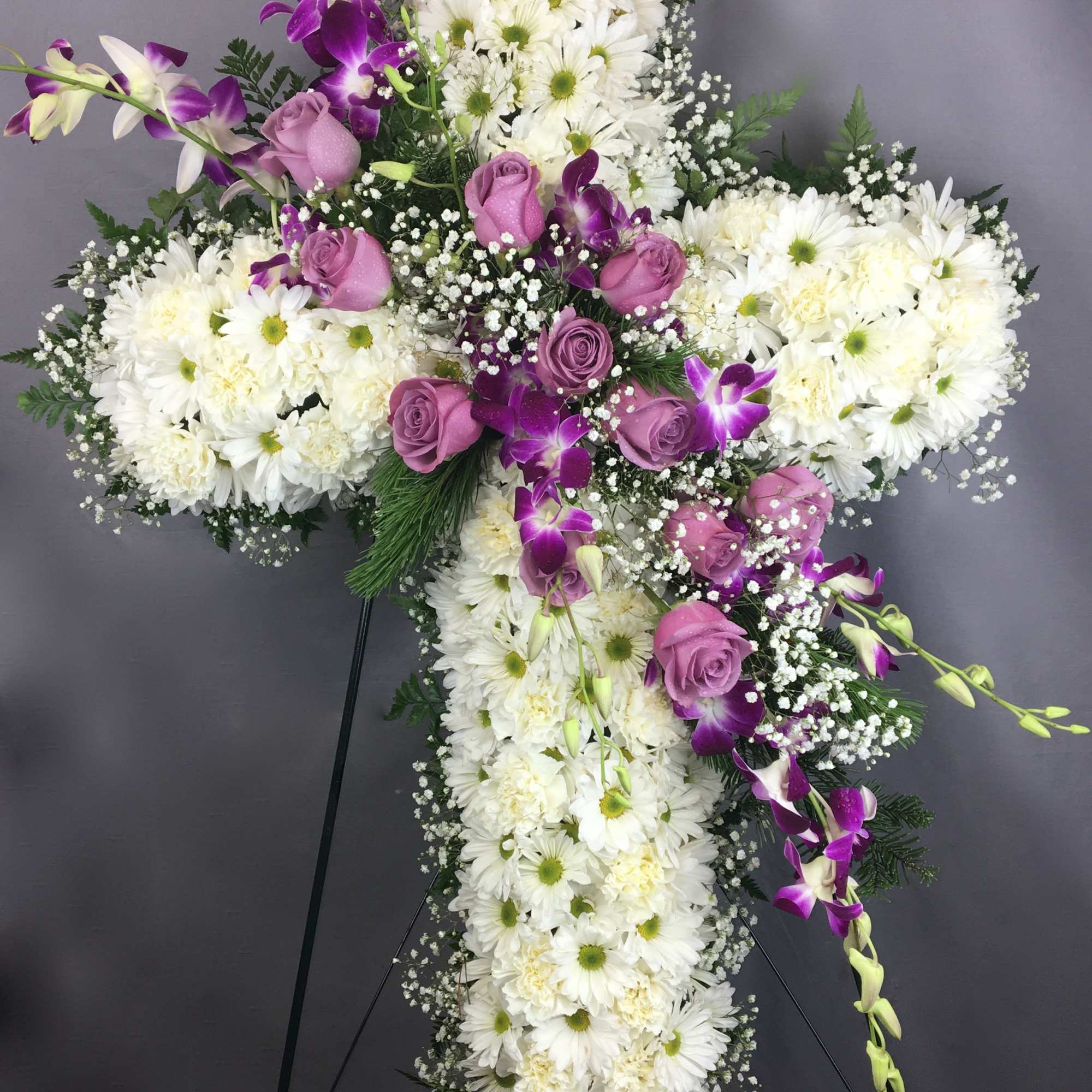 White floral cross with purple roses and orchids on a stand