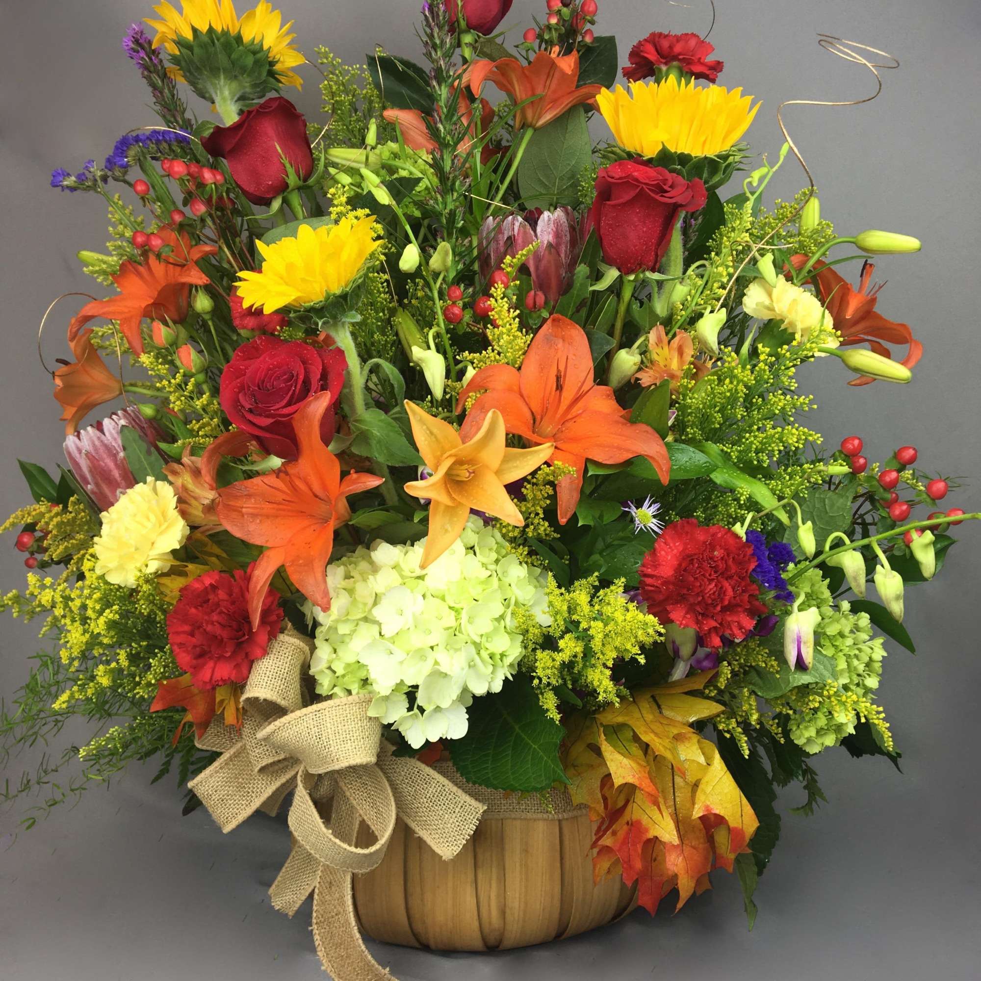 Autumn floral arrangement in a basket with roses, lilies, and sunflowers