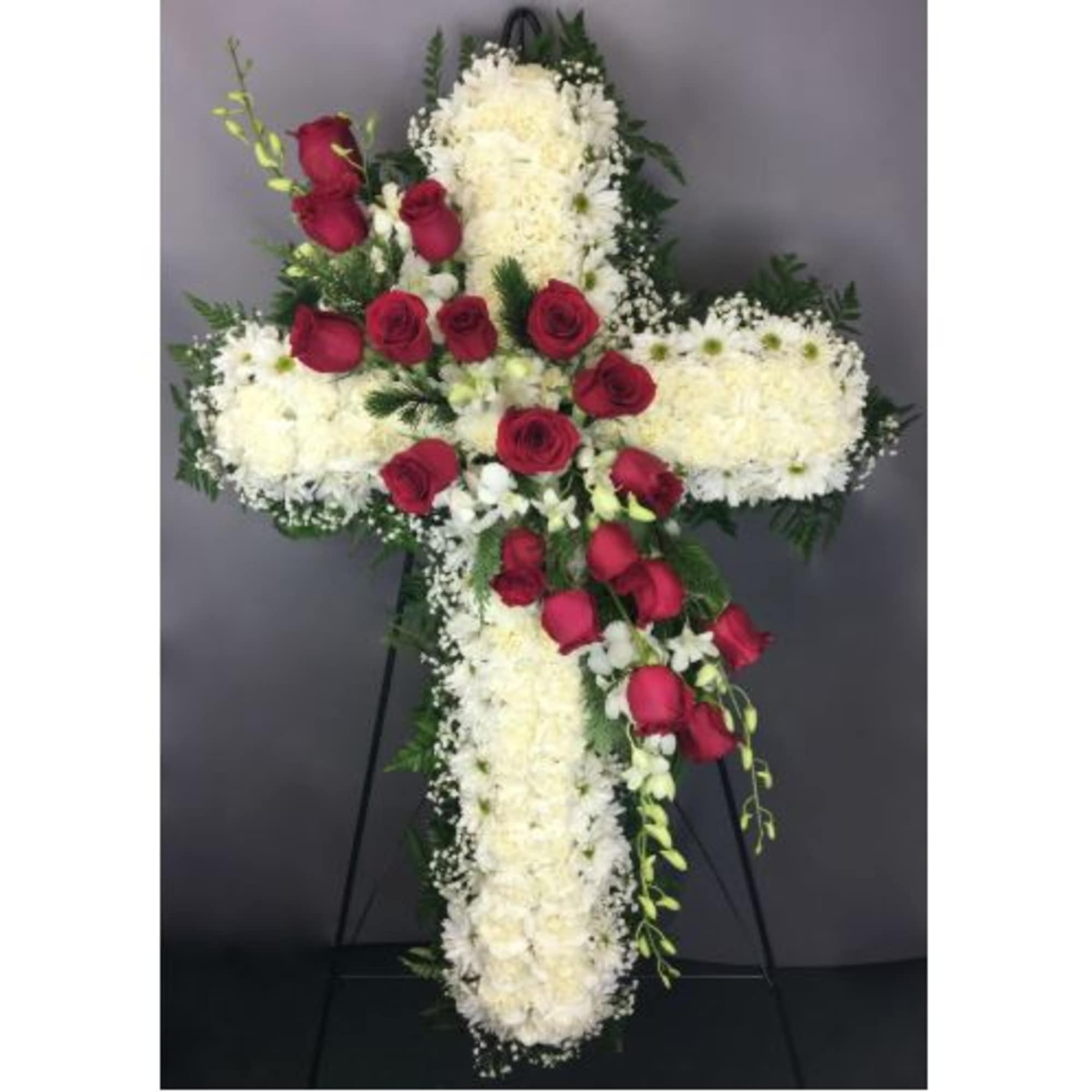 Cross-shaped floral arrangement with red roses and white flowers on an easel