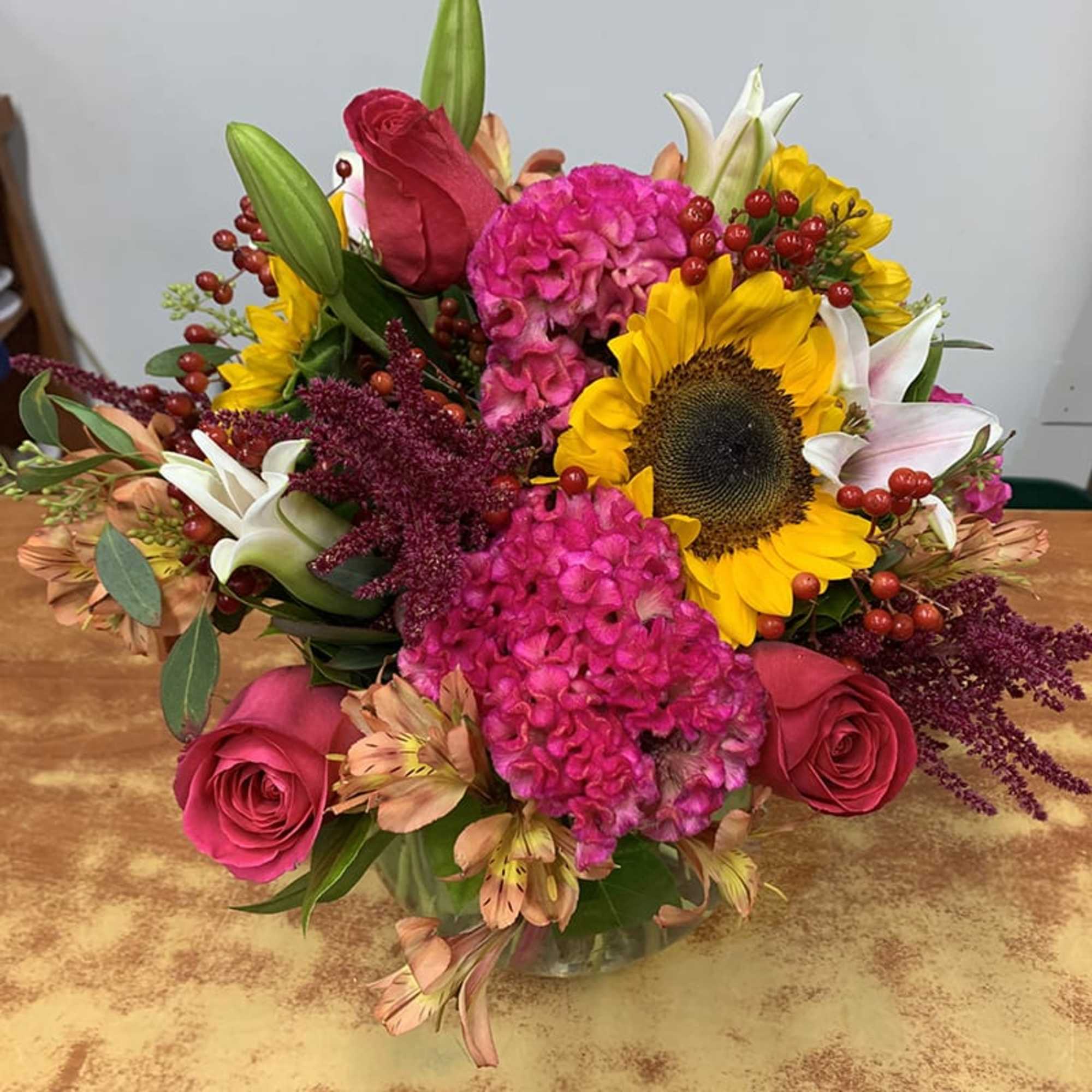 Bright mixed bouquet with sunflowers, pink roses, and lilies in a glass vase