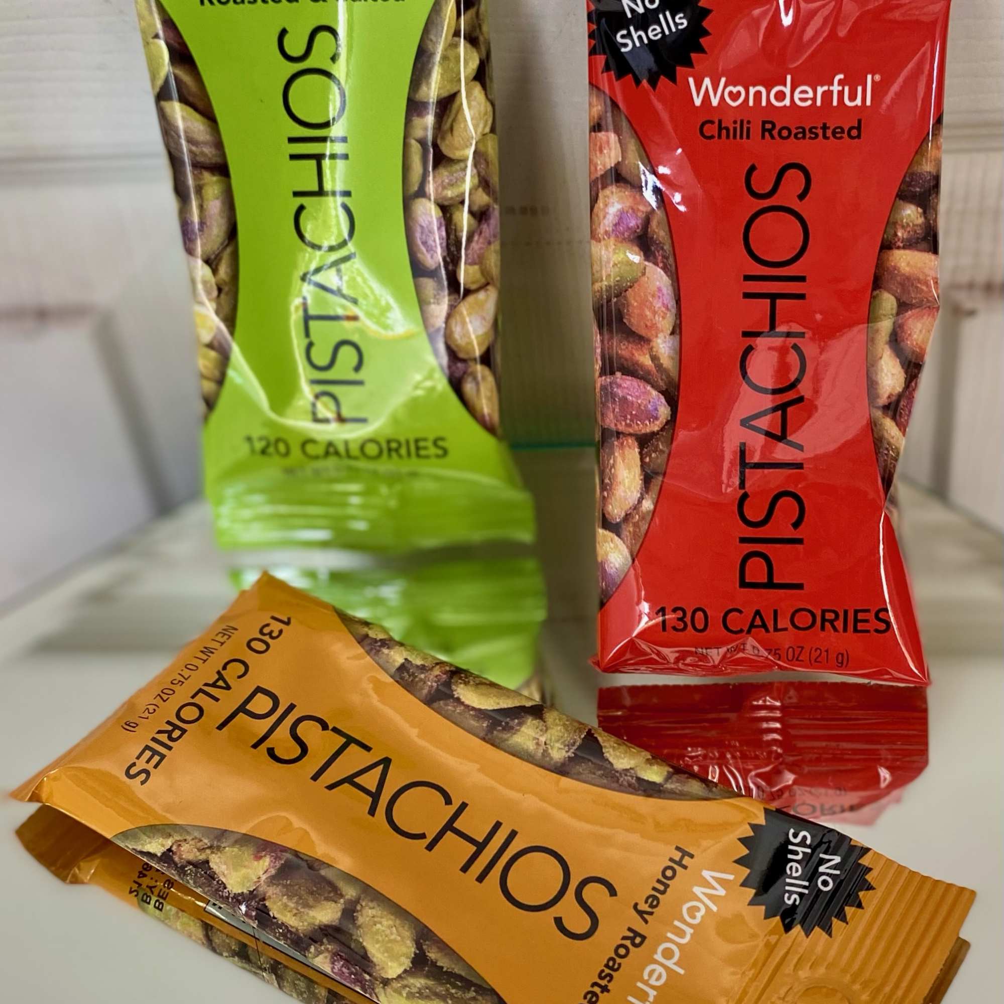 Three pistachio snack packs in green, red, and orange wrappers