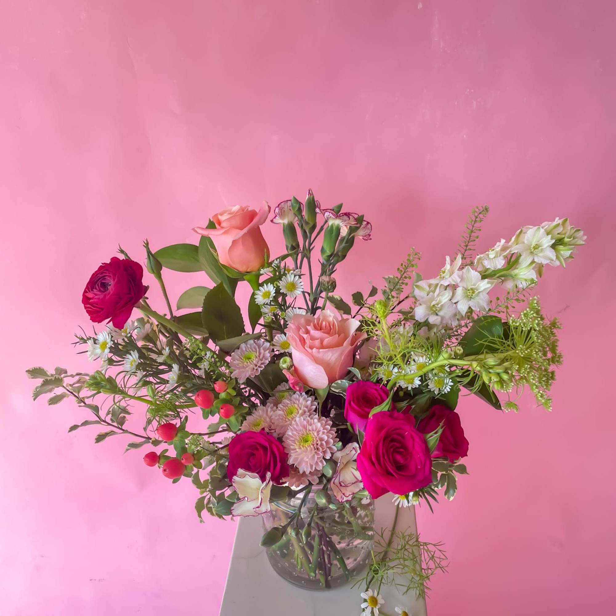 Mixed bouquet of pink roses, daisies, and white flowers in a glass vase