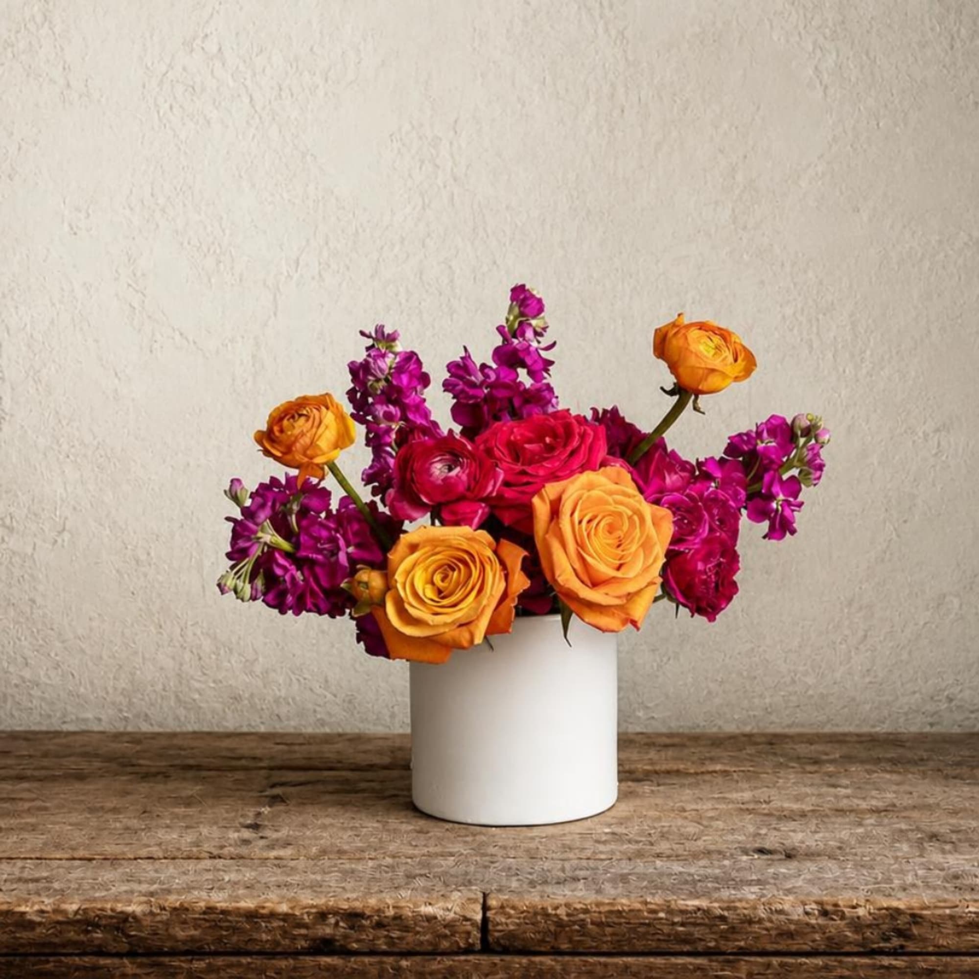 Orange and magenta flowers arranged in a white cylindrical vase
