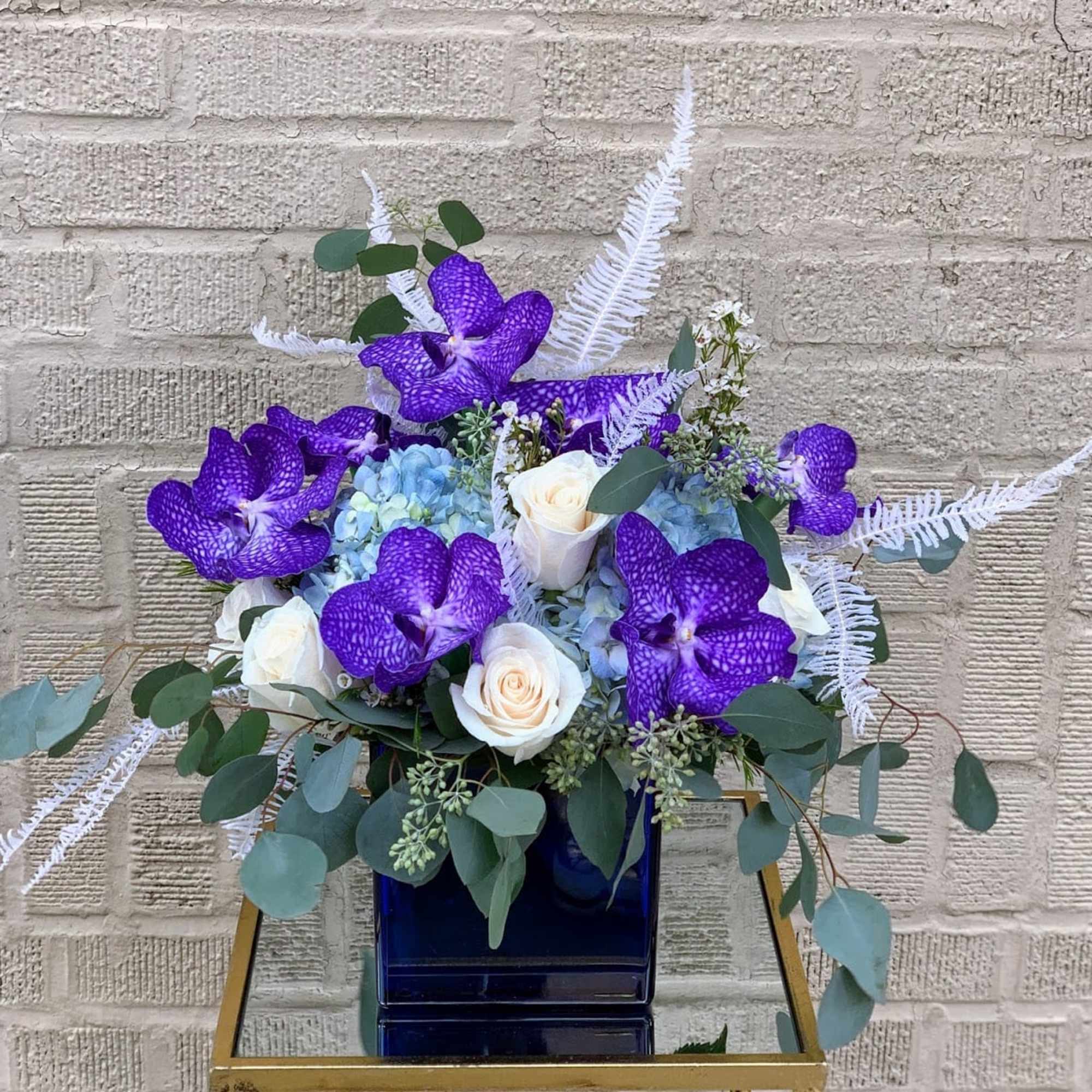 Purple orchids and white roses in a blue vase with airy greenery