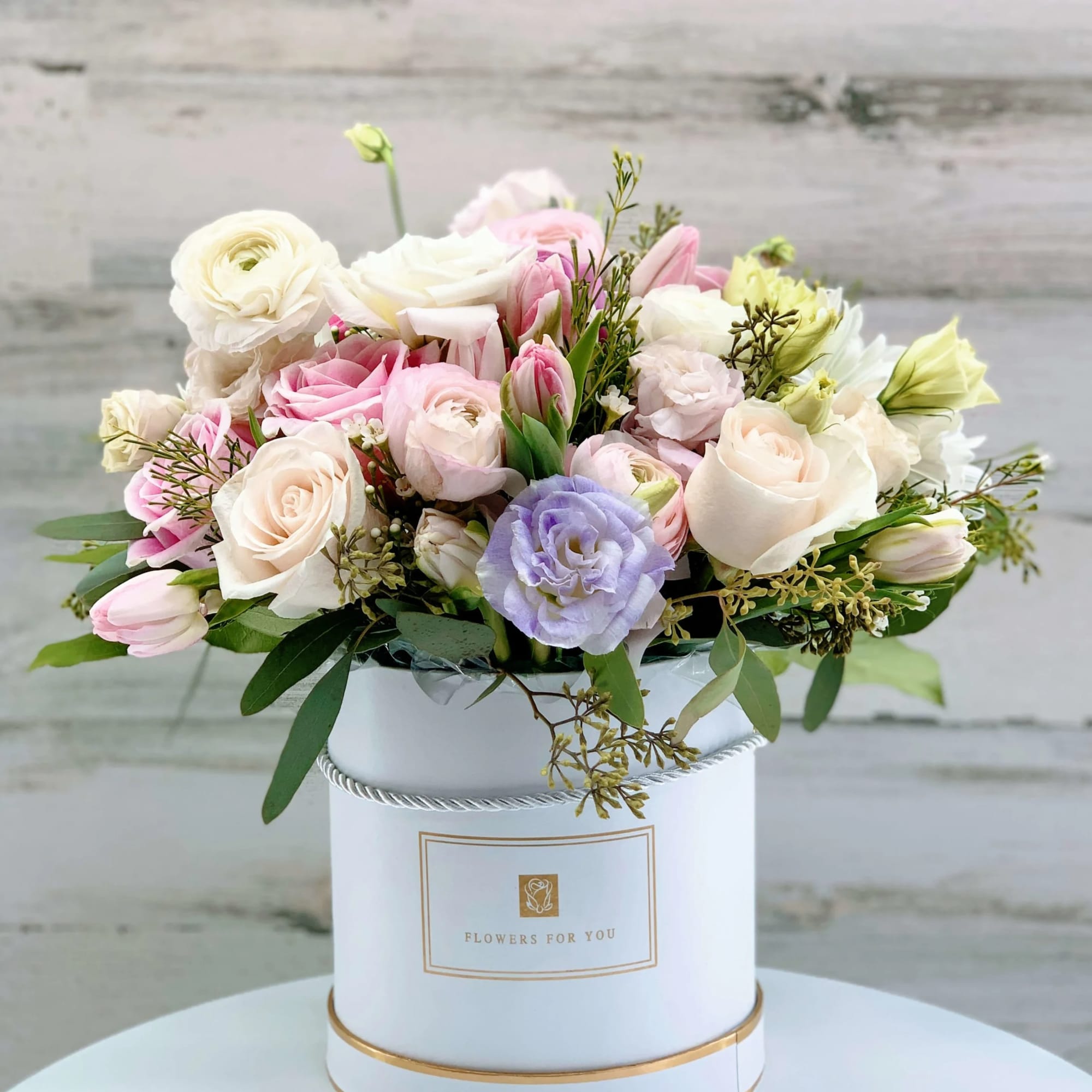Pastel roses and tulips arranged in a white hatbox
