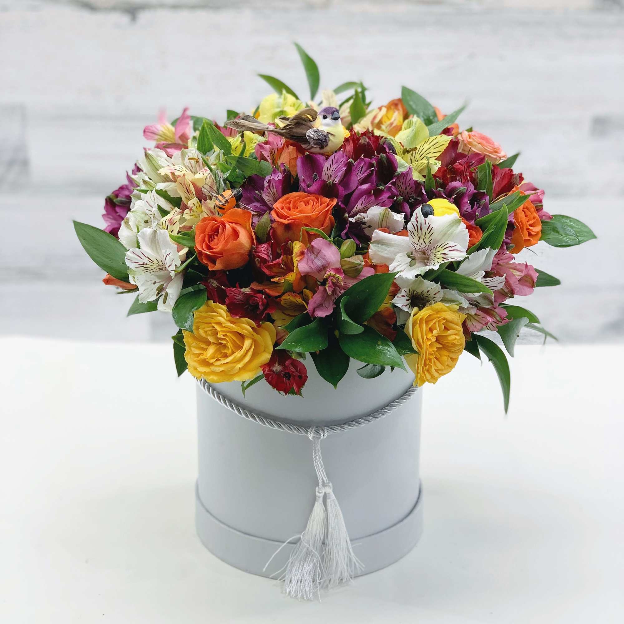 Mixed bouquet of orange, yellow, pink, and white flowers in a gray hat box