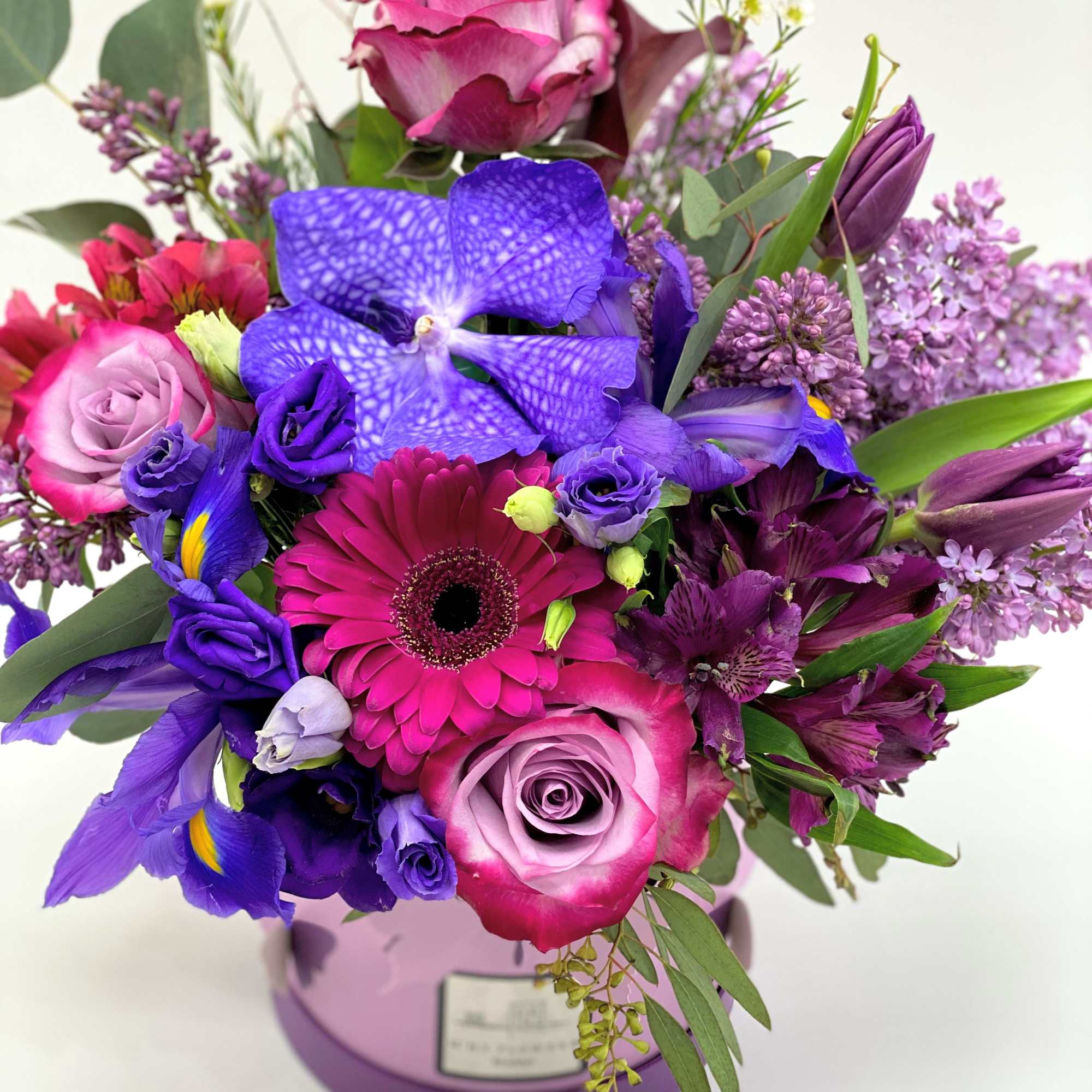 Mixed bouquet of pink, purple, and blue flowers in a lavender vase