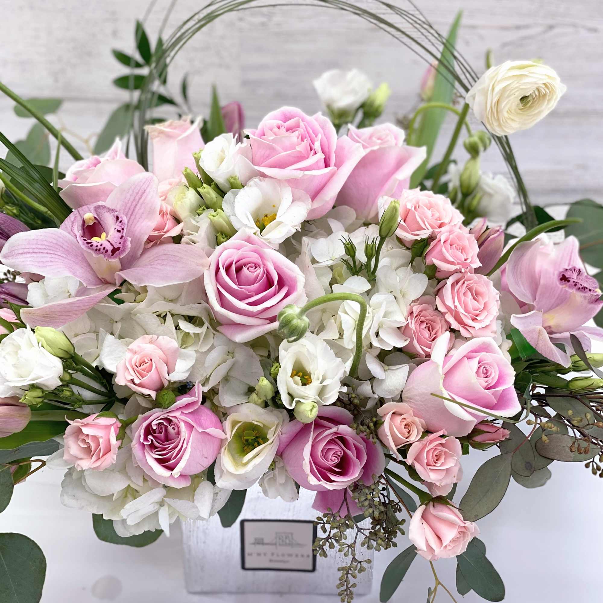 Pink roses and white blooms arranged in a white box with arching greenery