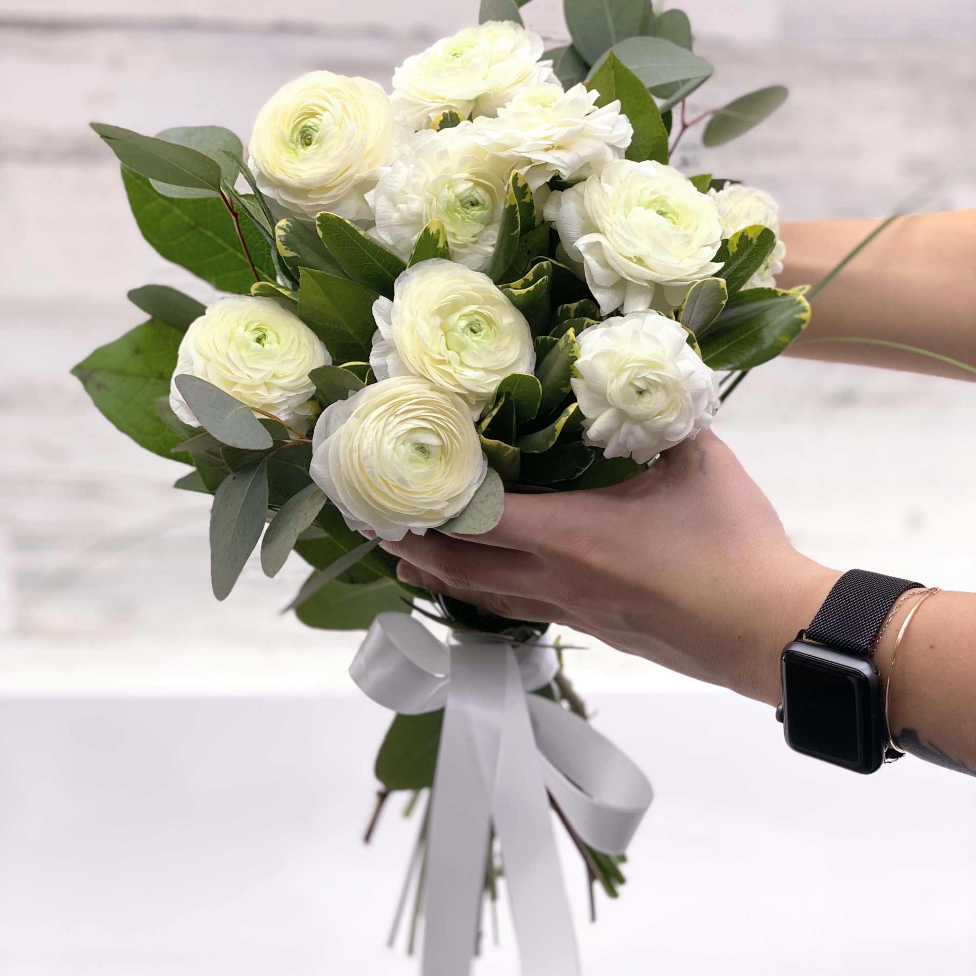 Hand-tied bouquet of white ranunculus with greenery and a white ribbon