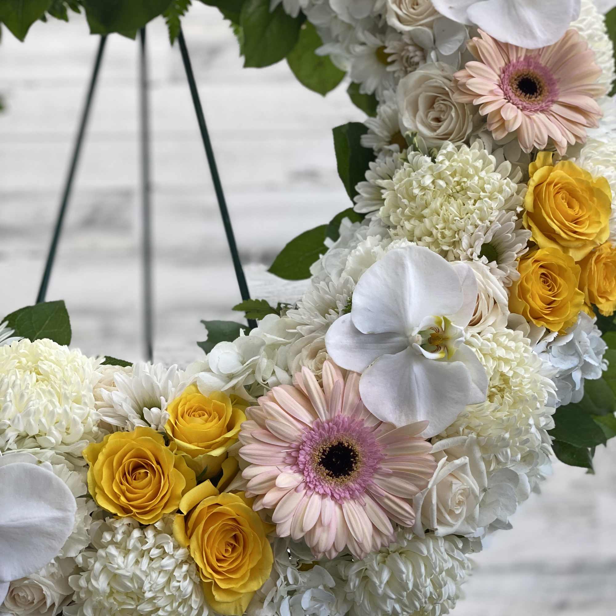 Floral wreath with white blooms, yellow roses, and pale pink gerbera daisies