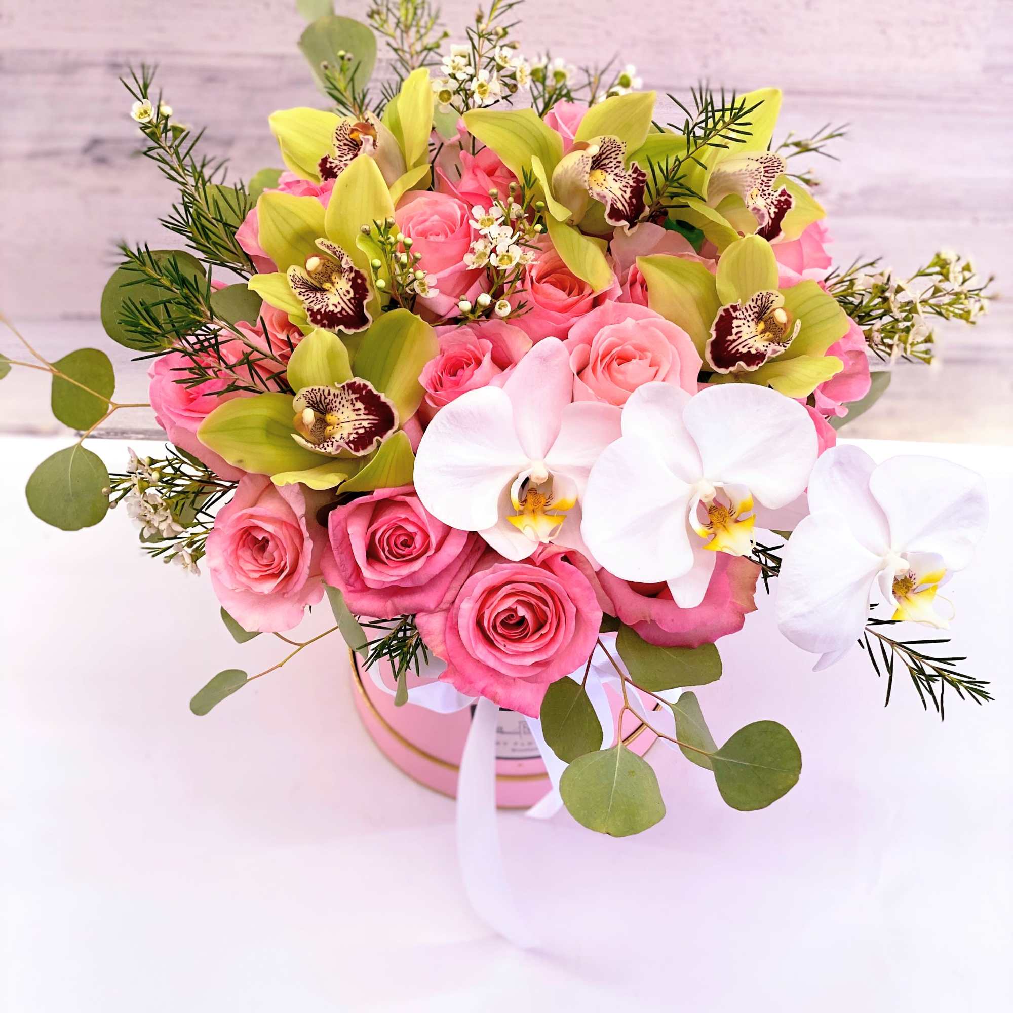Pink roses and white orchids in a round box arrangement