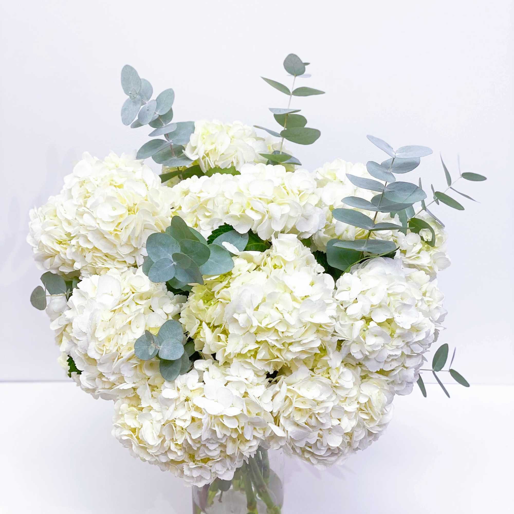White hydrangea bouquet in a clear glass vase with eucalyptus, photo 2 of 3