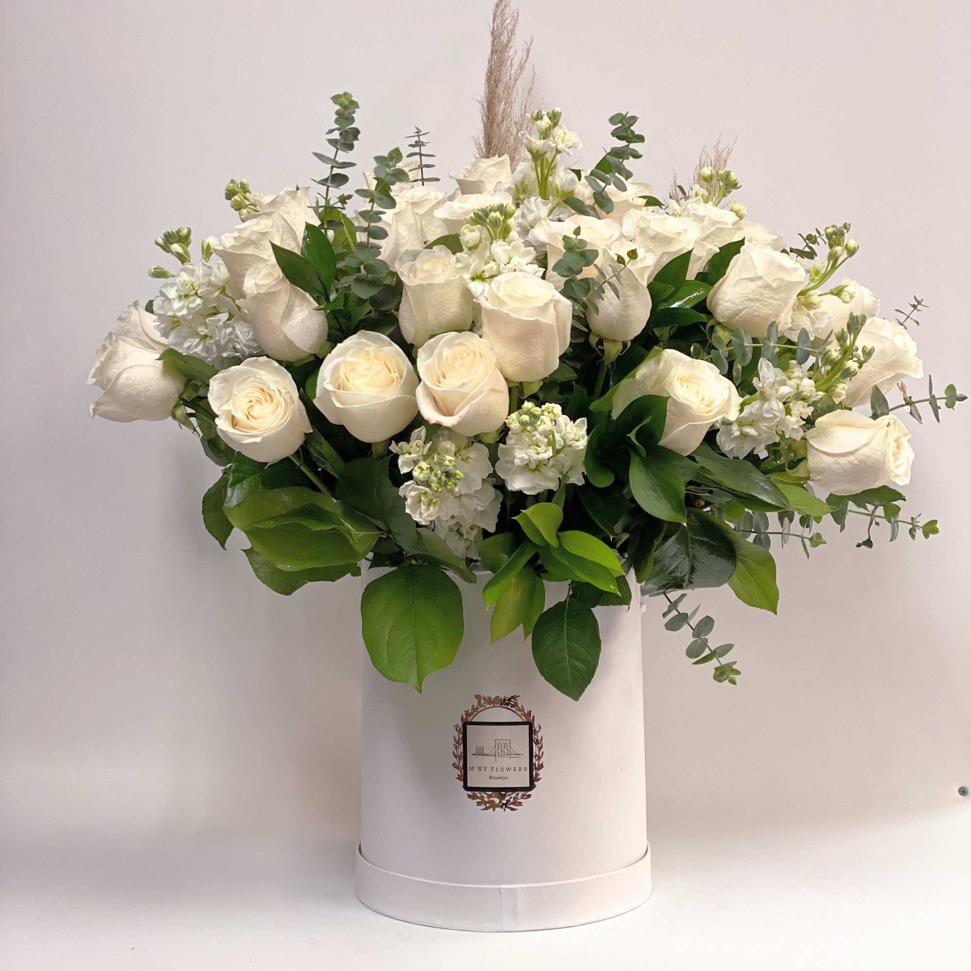 White roses and greenery arranged in a tall white hatbox