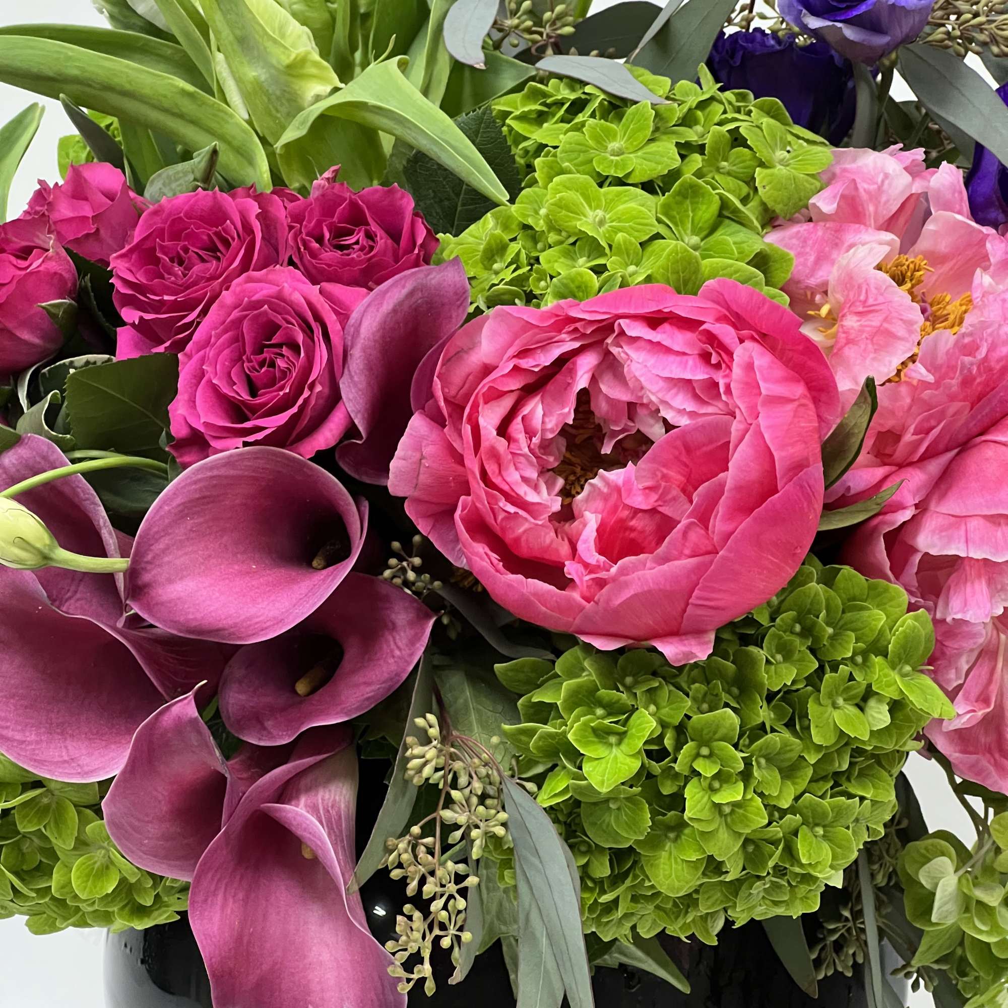 Bouquet of pink roses, purple calla lilies, and green hydrangeas in a black vase
