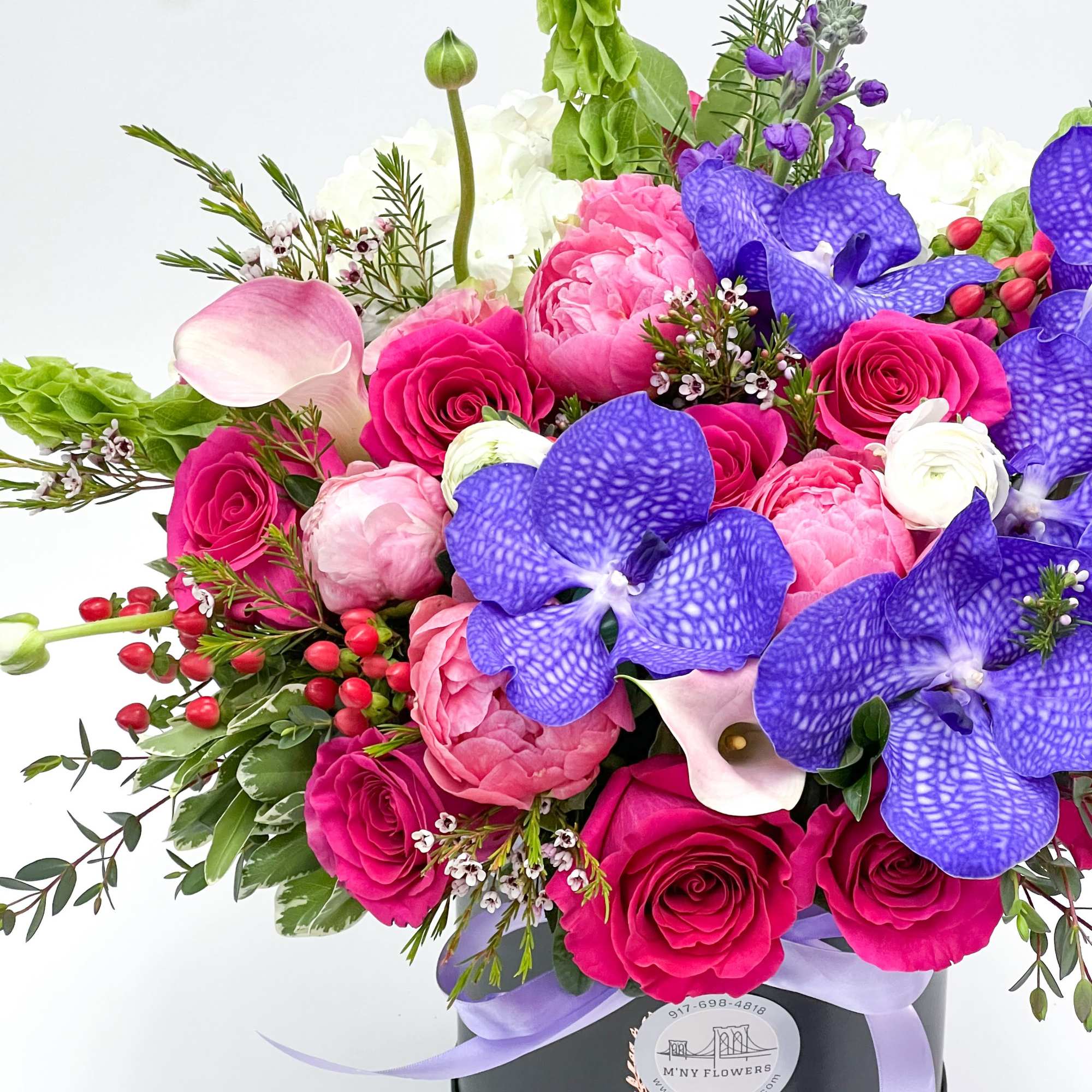 Bright mixed bouquet with pink roses, peonies, and purple orchids in a black hat box
