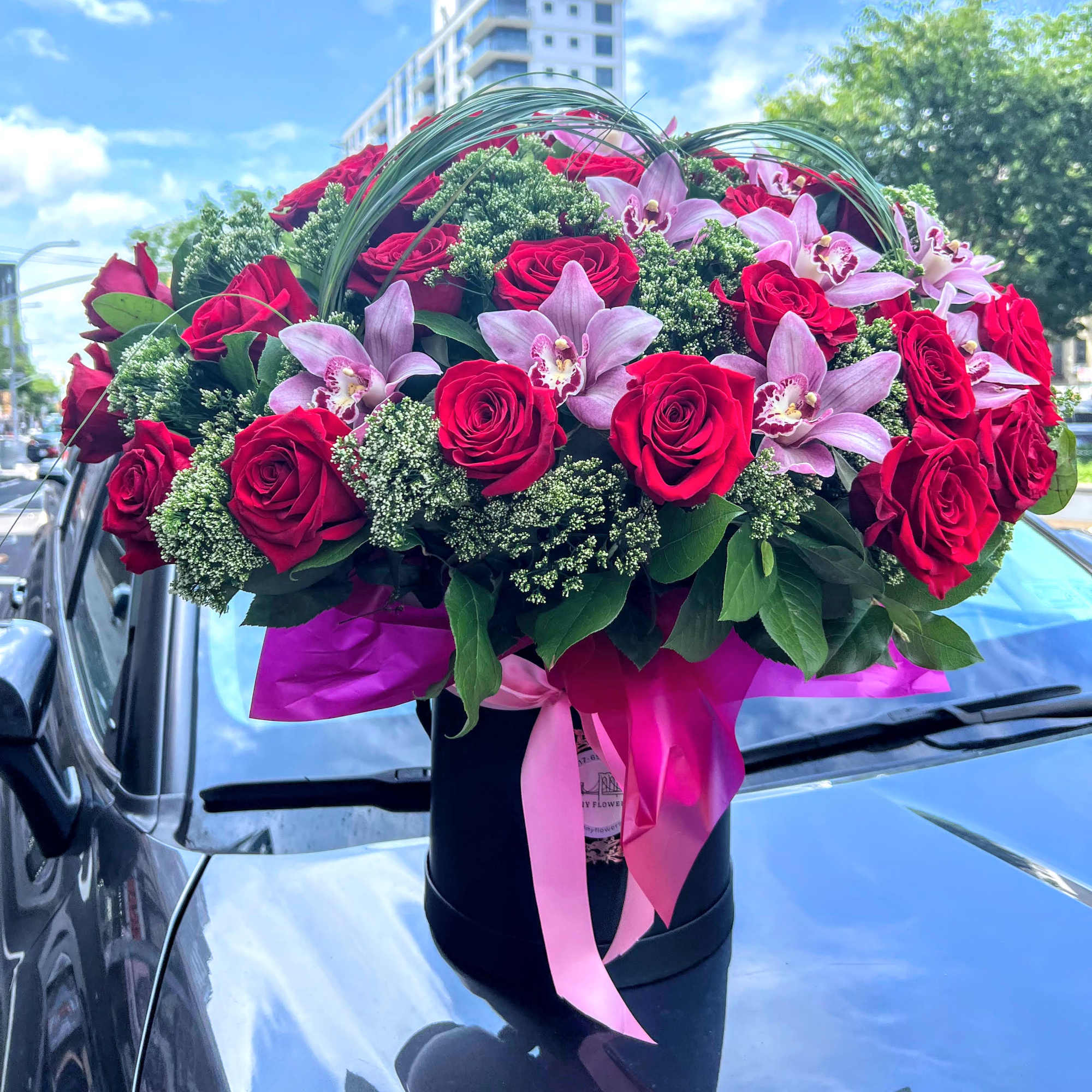 Bouquet of red roses and pink orchids in a black hat box with ribbon
