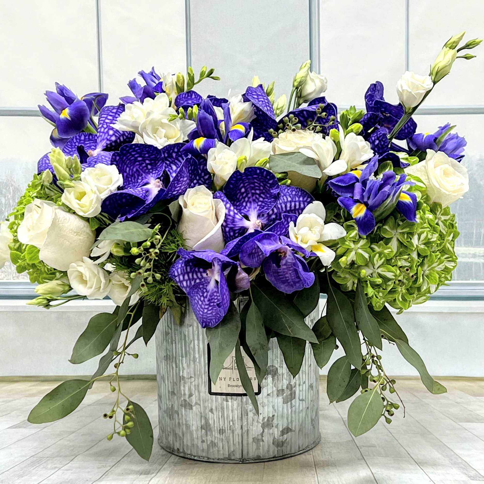 Purple and white floral arrangement in a metal container