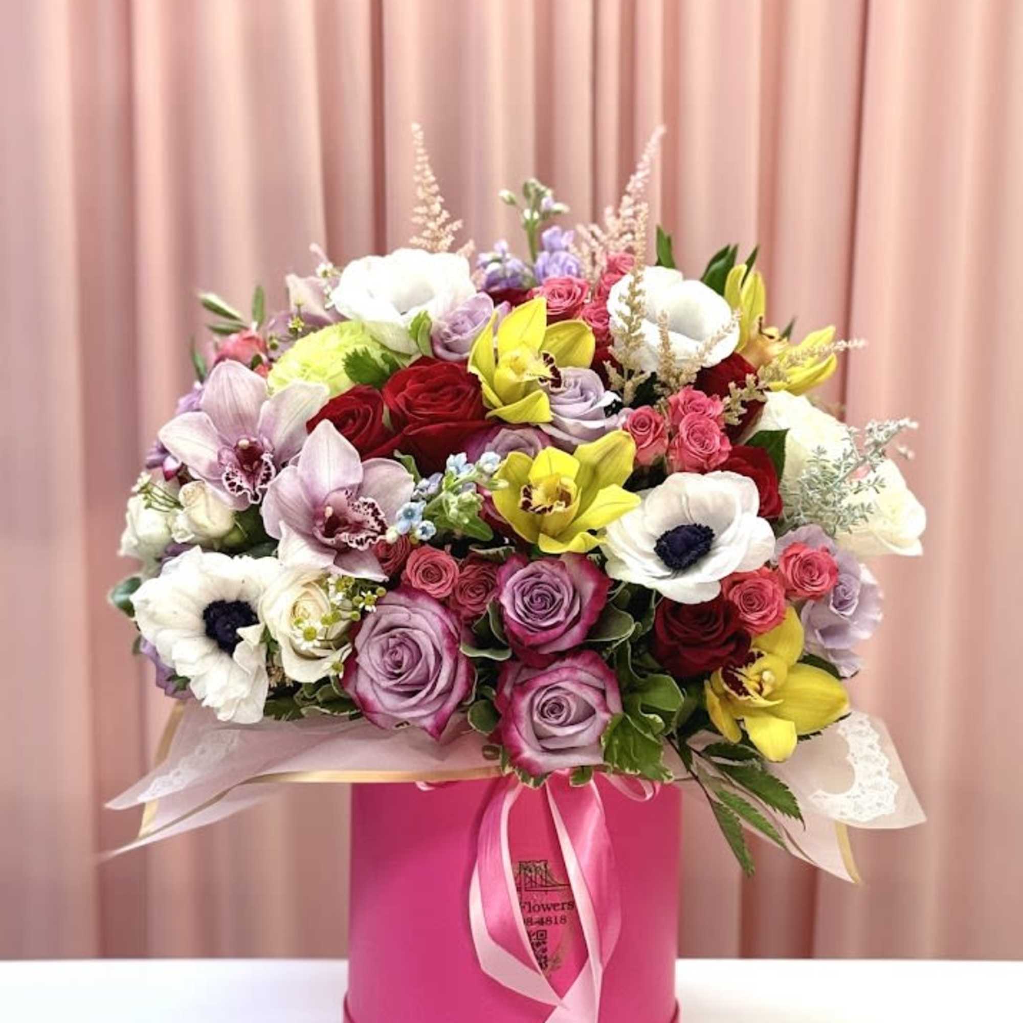 Mixed bouquet of roses, orchids, and anemones in a pink hat box
