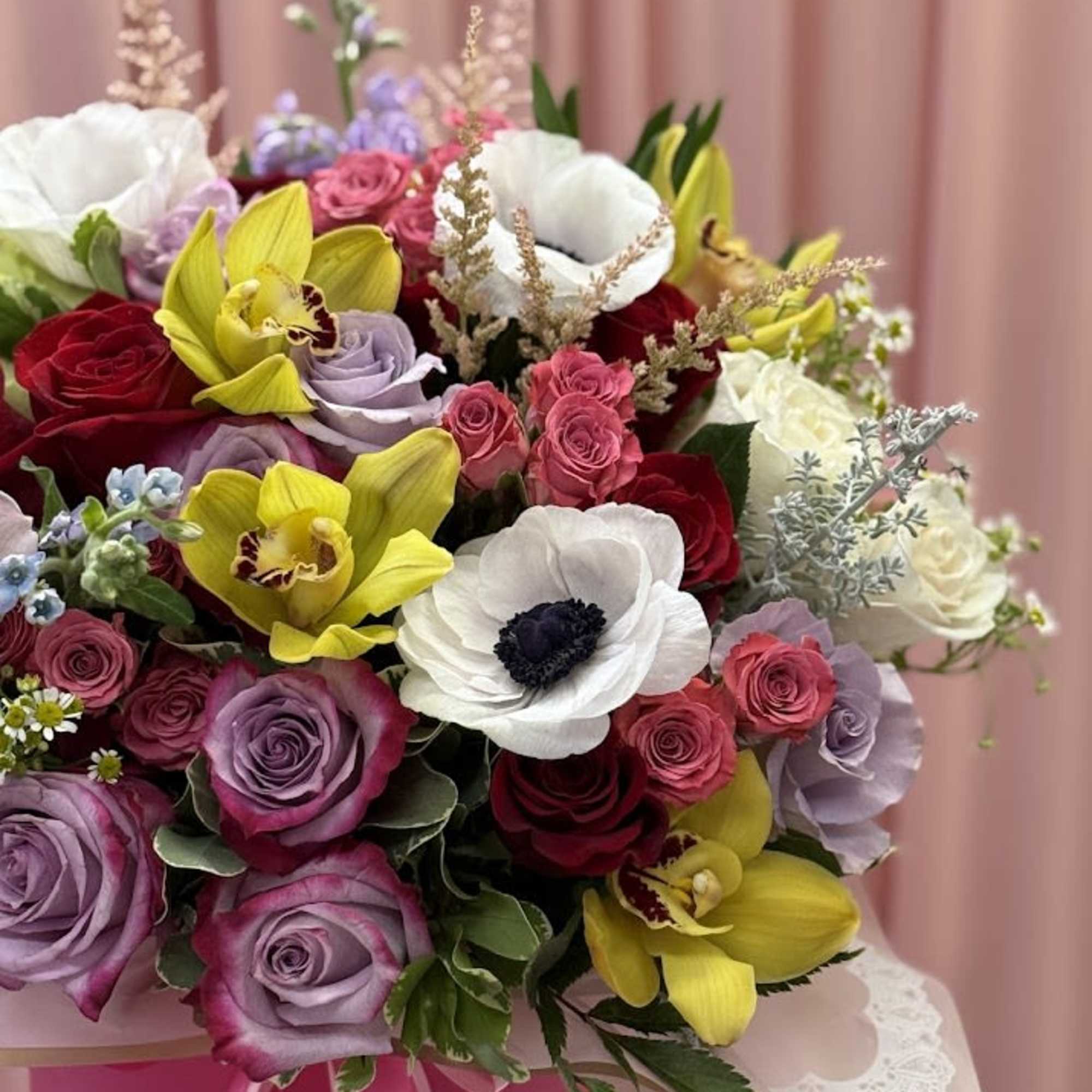 Bouquet of roses and orchids with white anemones in pink wrapping