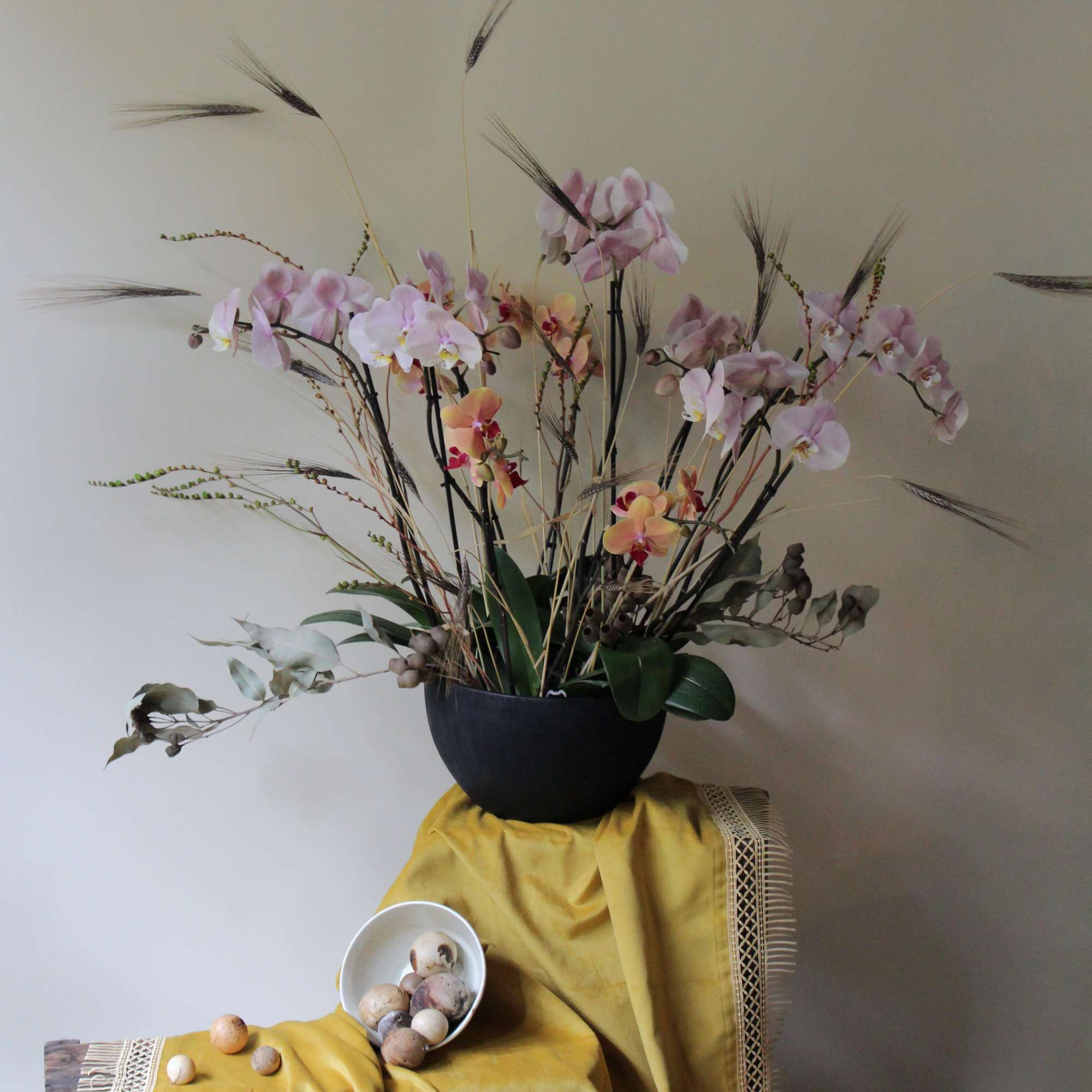 Pink orchid arrangement in a black bowl with tall dried stems