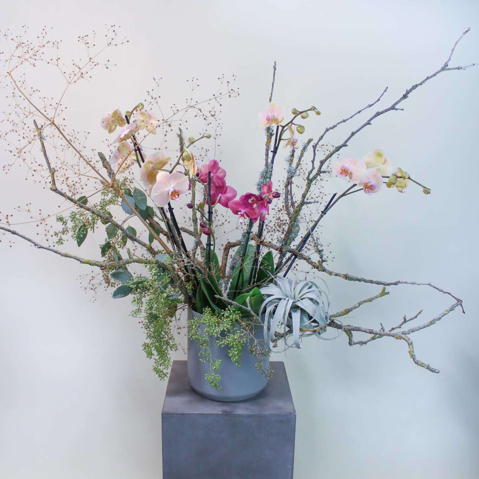 Tall orchid arrangement in a gray vase with branching twigs