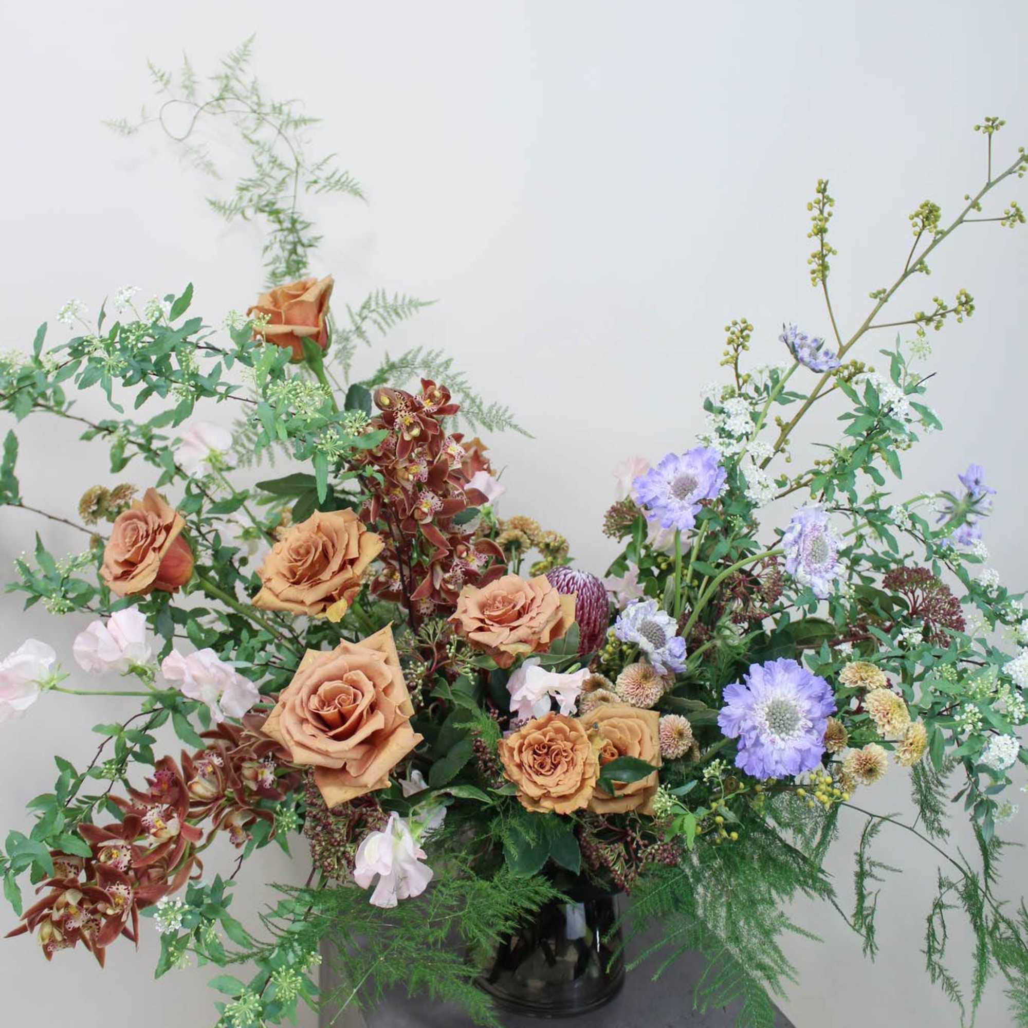 Large mixed floral arrangement in a black vase with peach and lavender blooms
