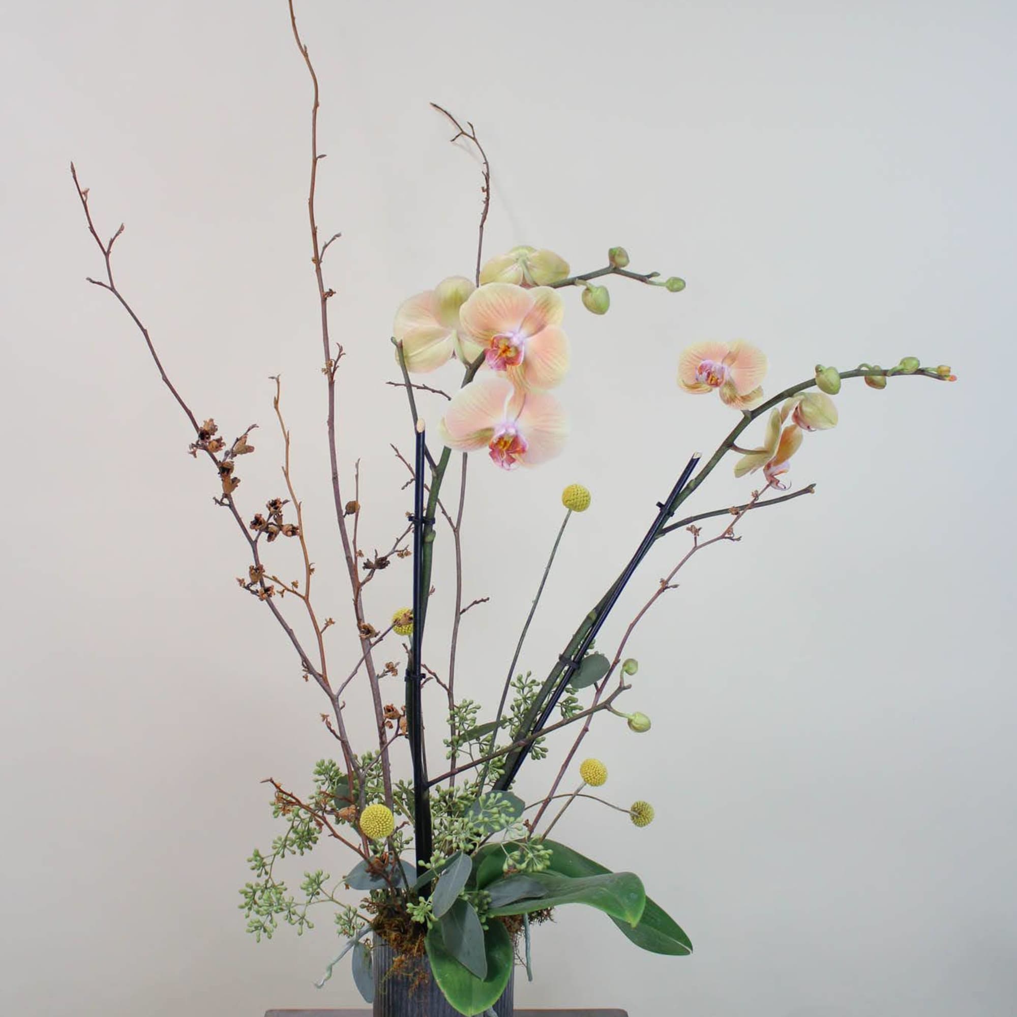 Tall orchid arrangement in a ribbed metal vase with branches and round yellow accents