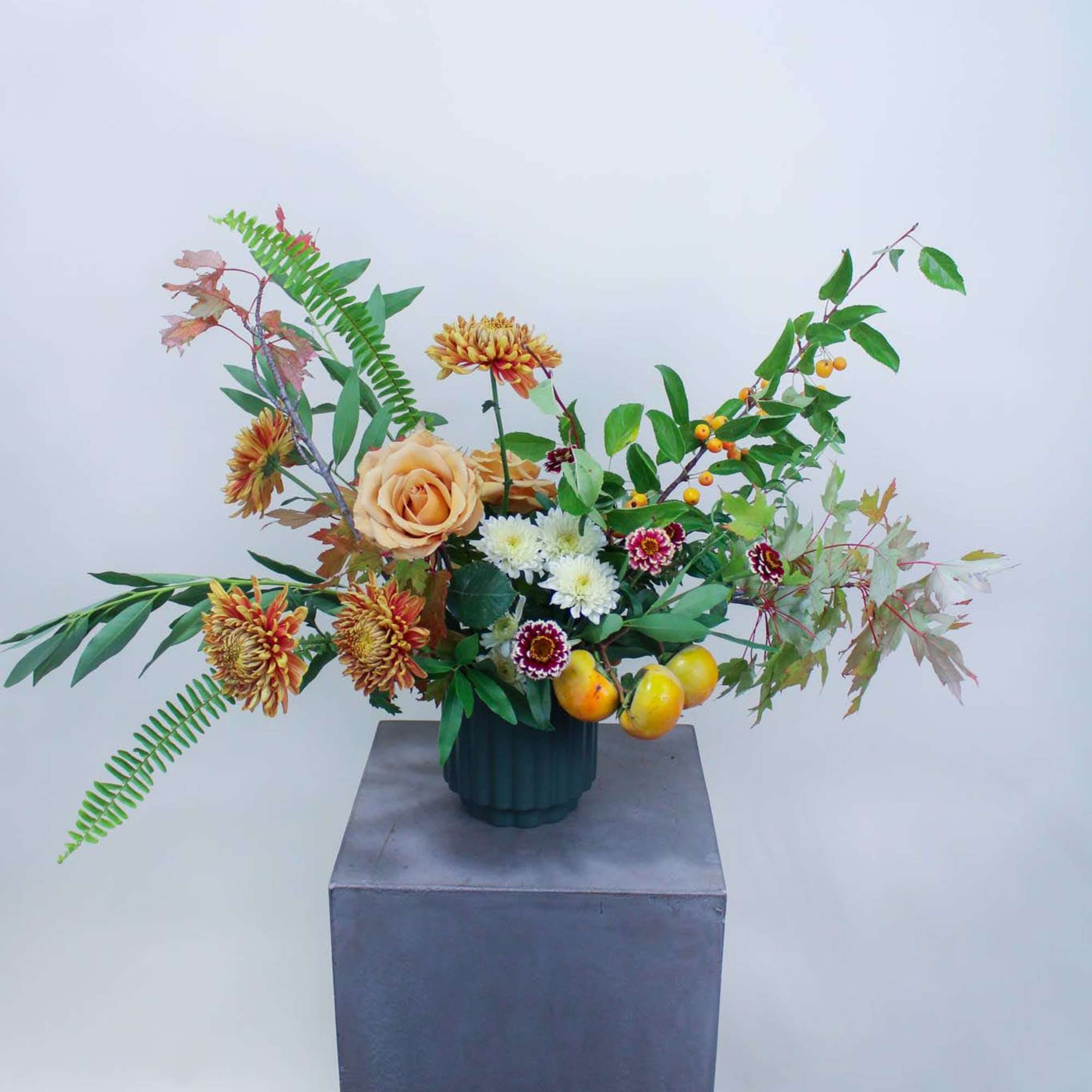 Mixed floral arrangement in a dark vase with peach roses and orange chrysanthemums