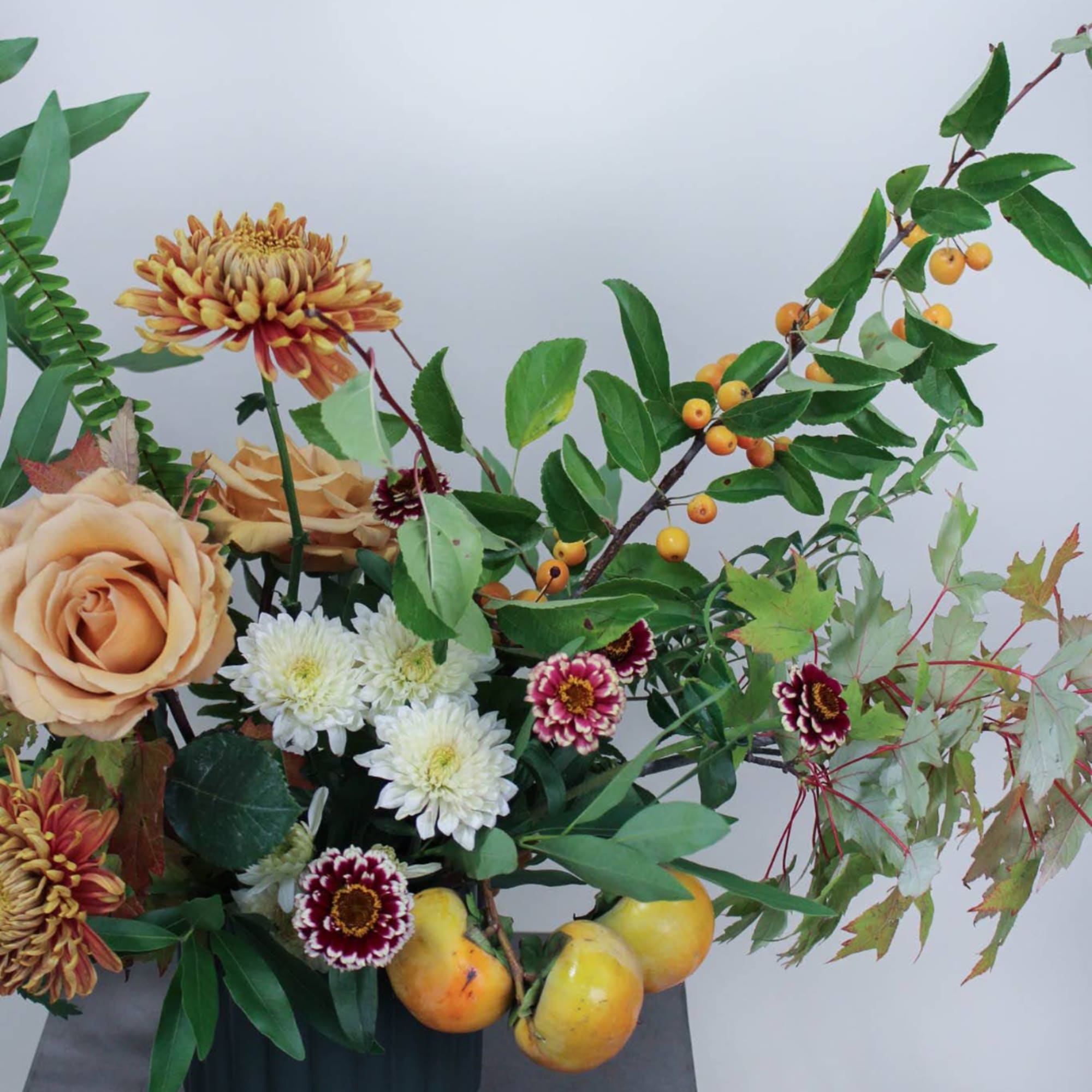 Mixed floral arrangement with peach roses, white chrysanthemums, and berries in a dark vase