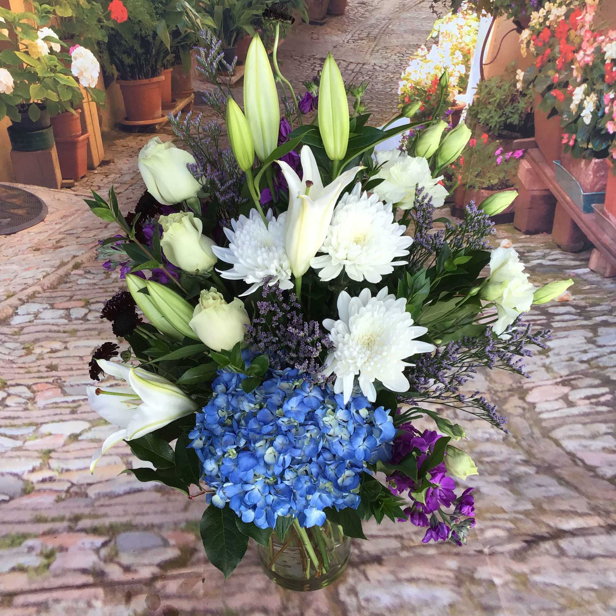 Bouquet of white lilies, white chrysanthemums, and blue hydrangea in a glass vase