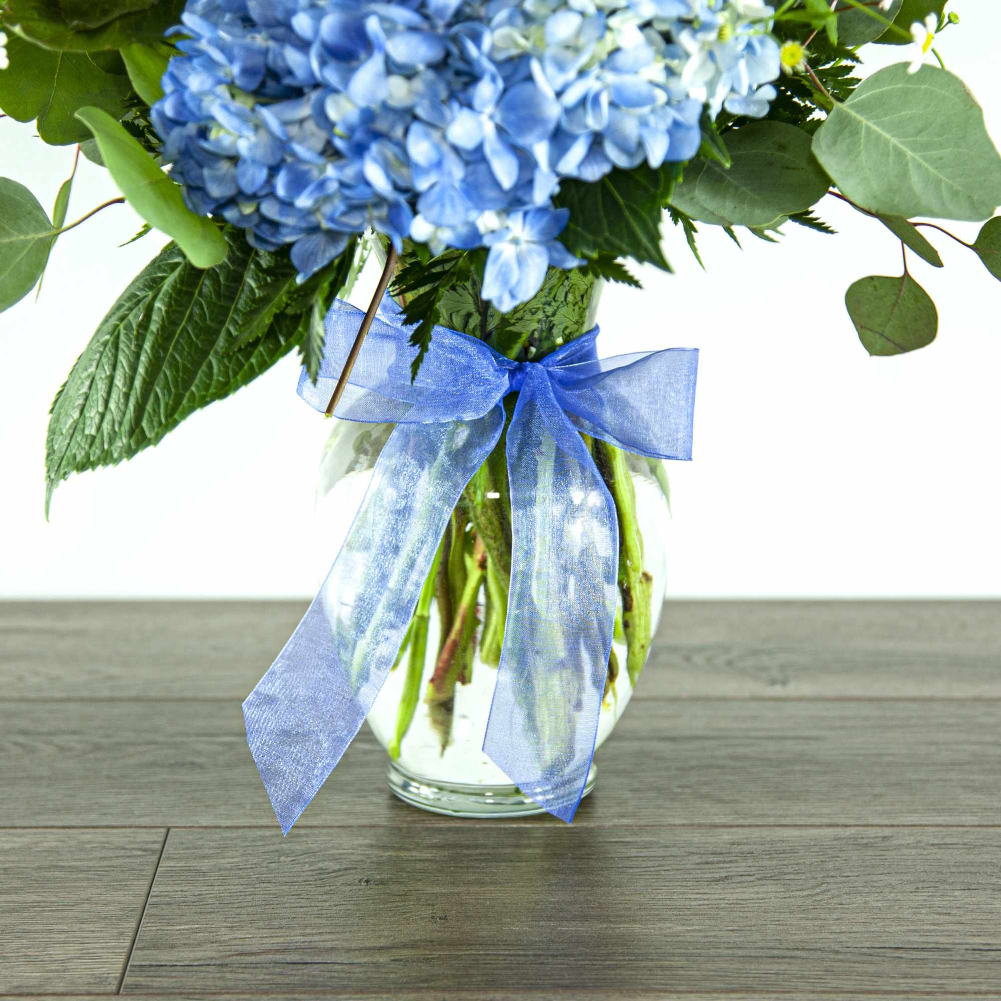 Blue hydrangea bouquet in a glass vase with a blue ribbon