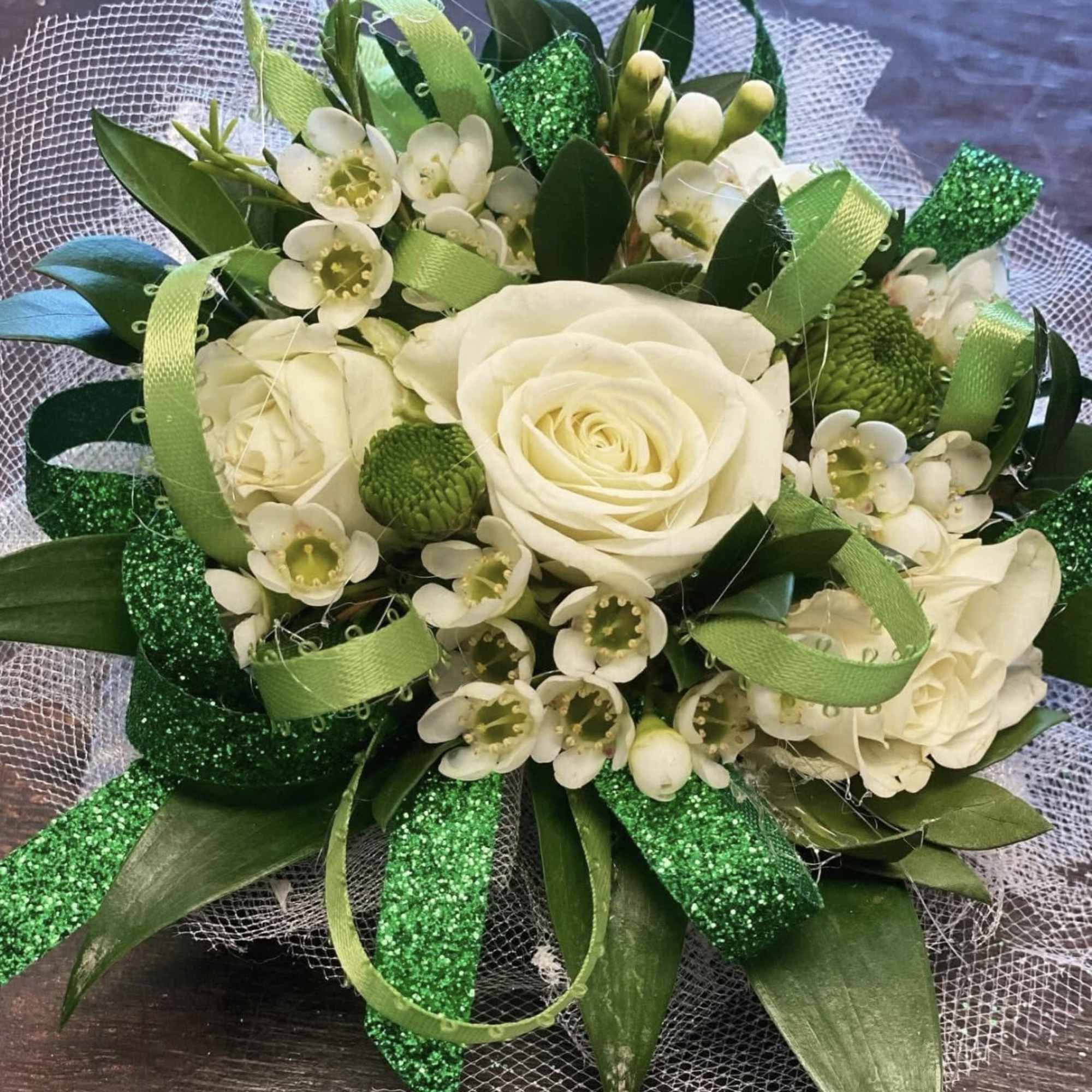 A timeless corsage featuring a pristine white rose nestled among fresh, lush