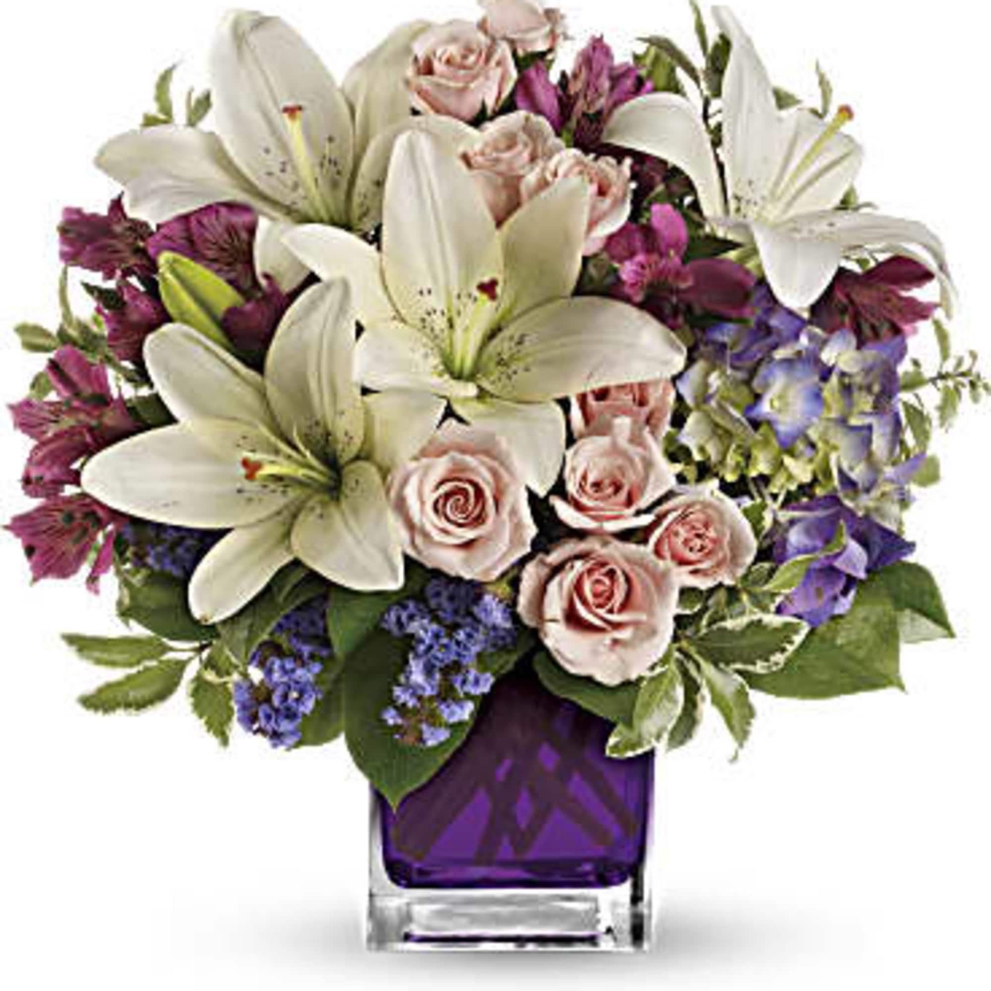 Bouquet of white lilies, pink roses, and purple flowers in a purple glass vase