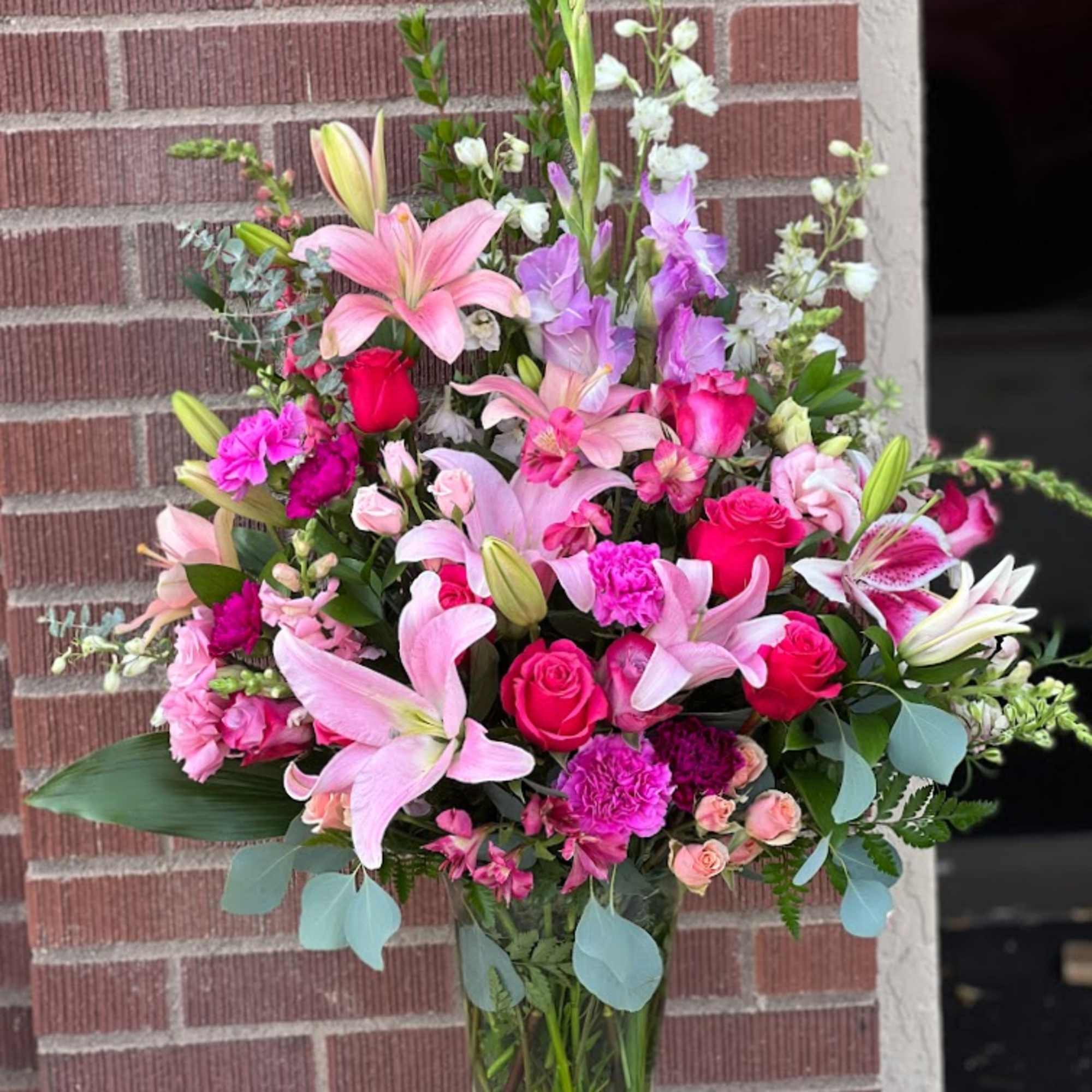 Tall bouquet of pink lilies, roses, and purple blooms in a glass vase