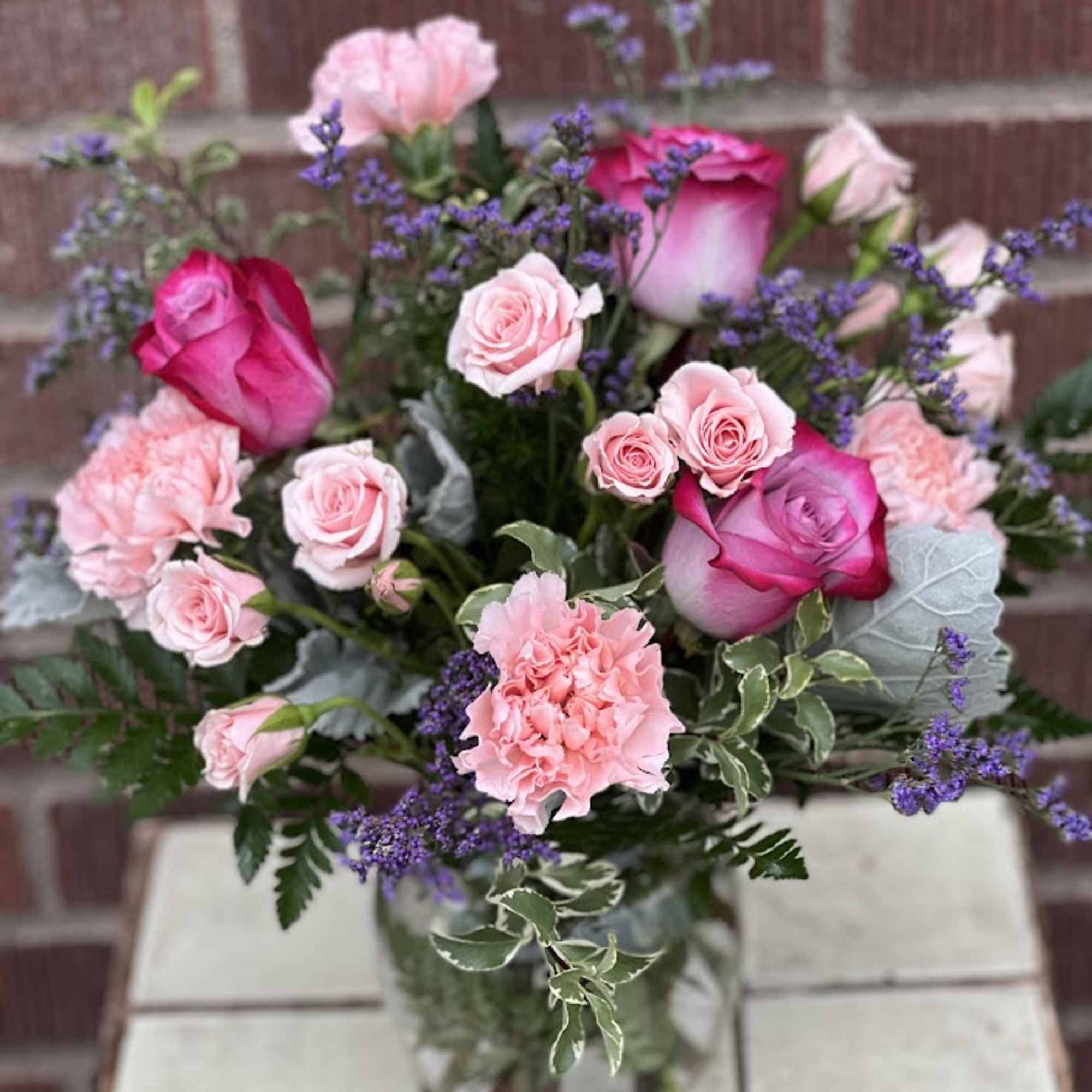 Pink roses and carnations arranged in a glass vase with purple filler flowers.