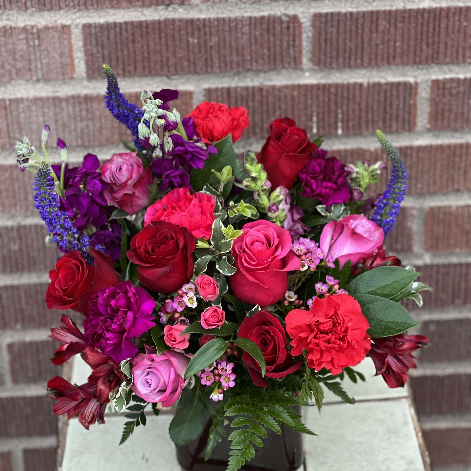 Mixed bouquet of red, pink, and purple flowers in a dark vase