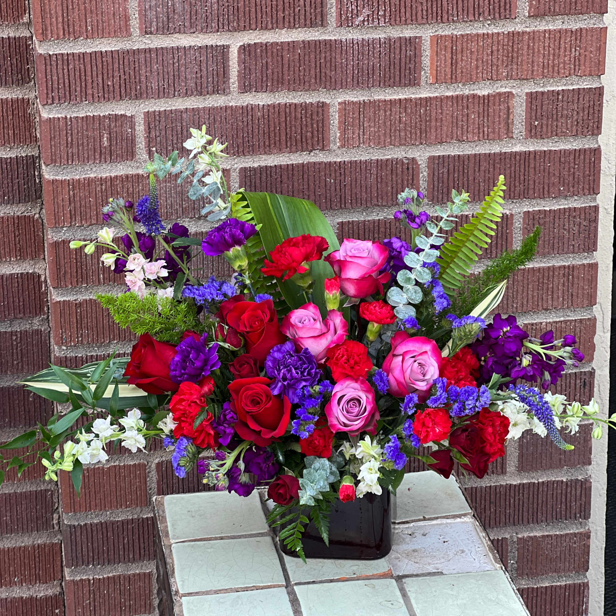 Mixed bouquet of red, pink, purple, and white flowers in a black vase