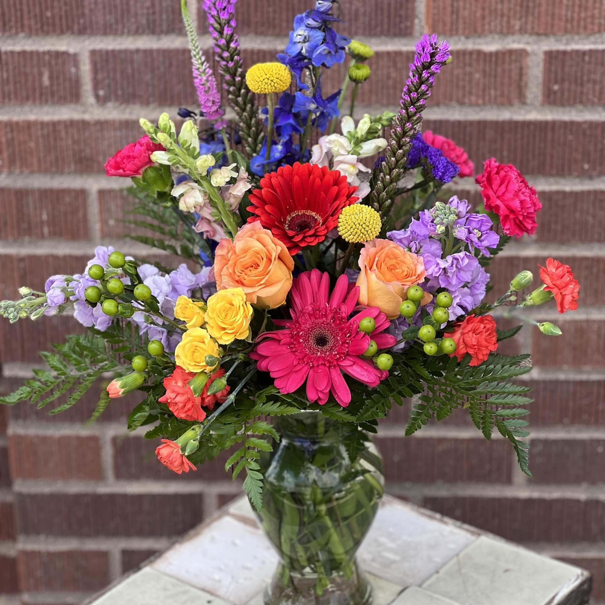 Colorful mixed bouquet in a glass vase with gerbera daisies, roses, and snapdragons.