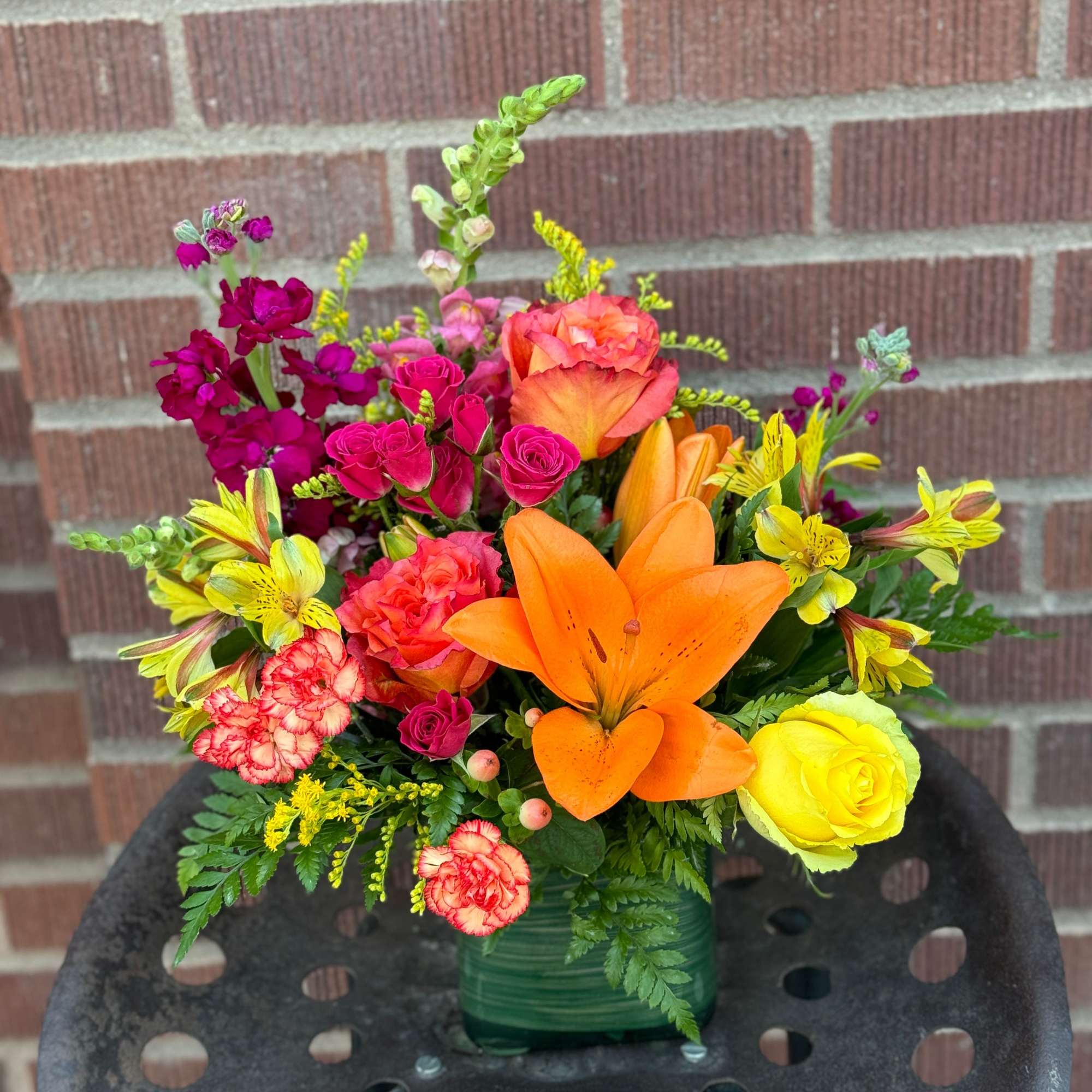 Bright mixed bouquet with orange lilies, pink roses, and yellow blooms in a green vase
