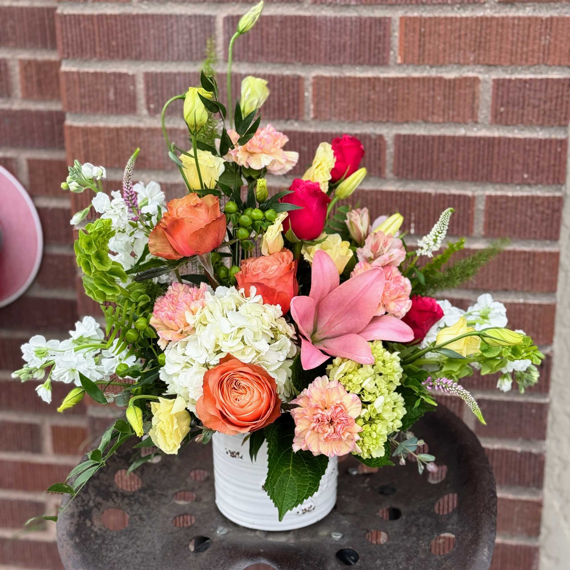 Mixed bouquet in a white container with pink, orange, yellow, and white blooms