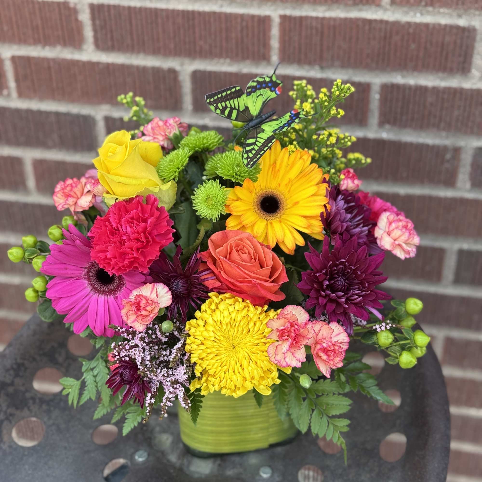 Colorful mixed bouquet in a green vase with butterfly picks