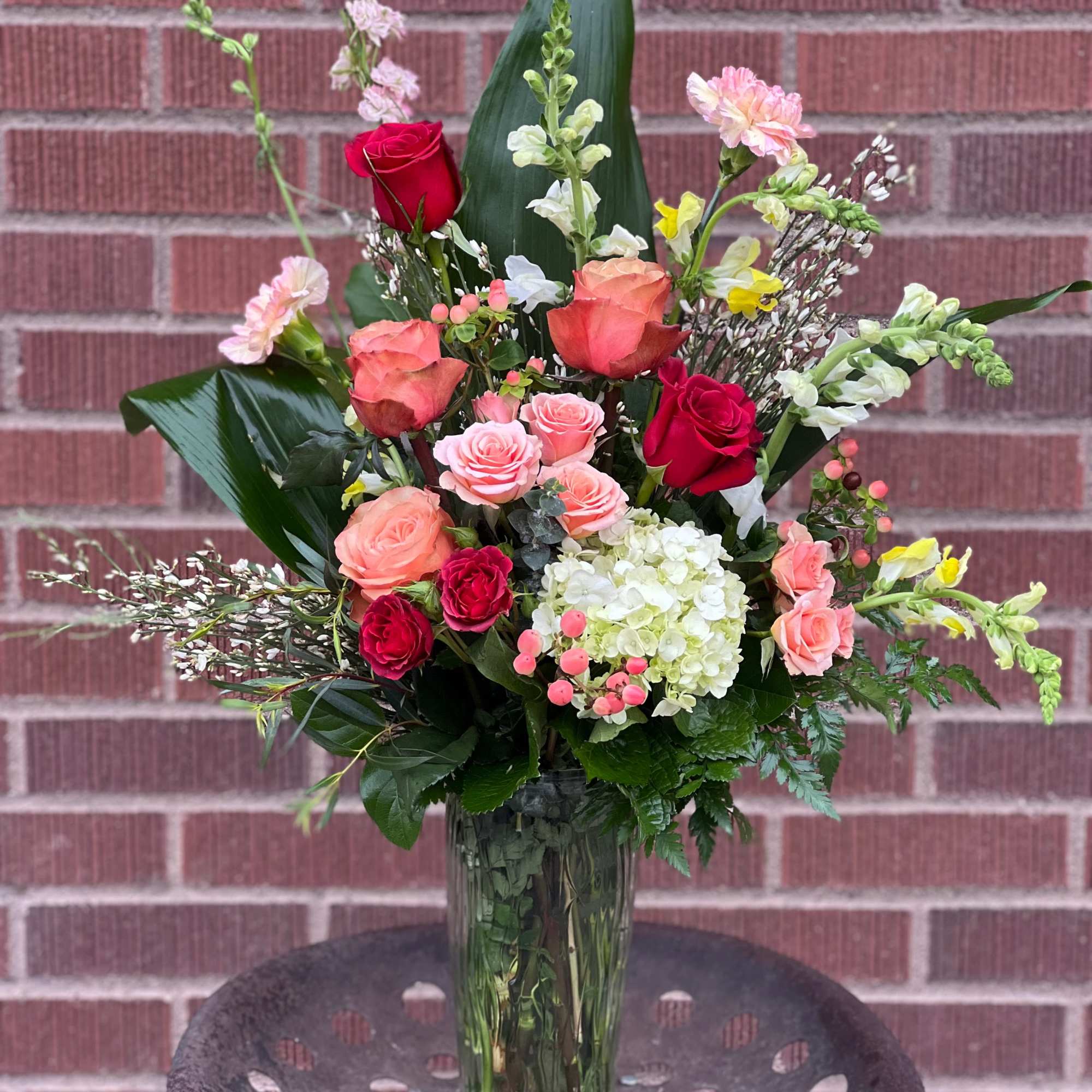 Mixed bouquet of roses, hydrangea, and snapdragons in a glass vase