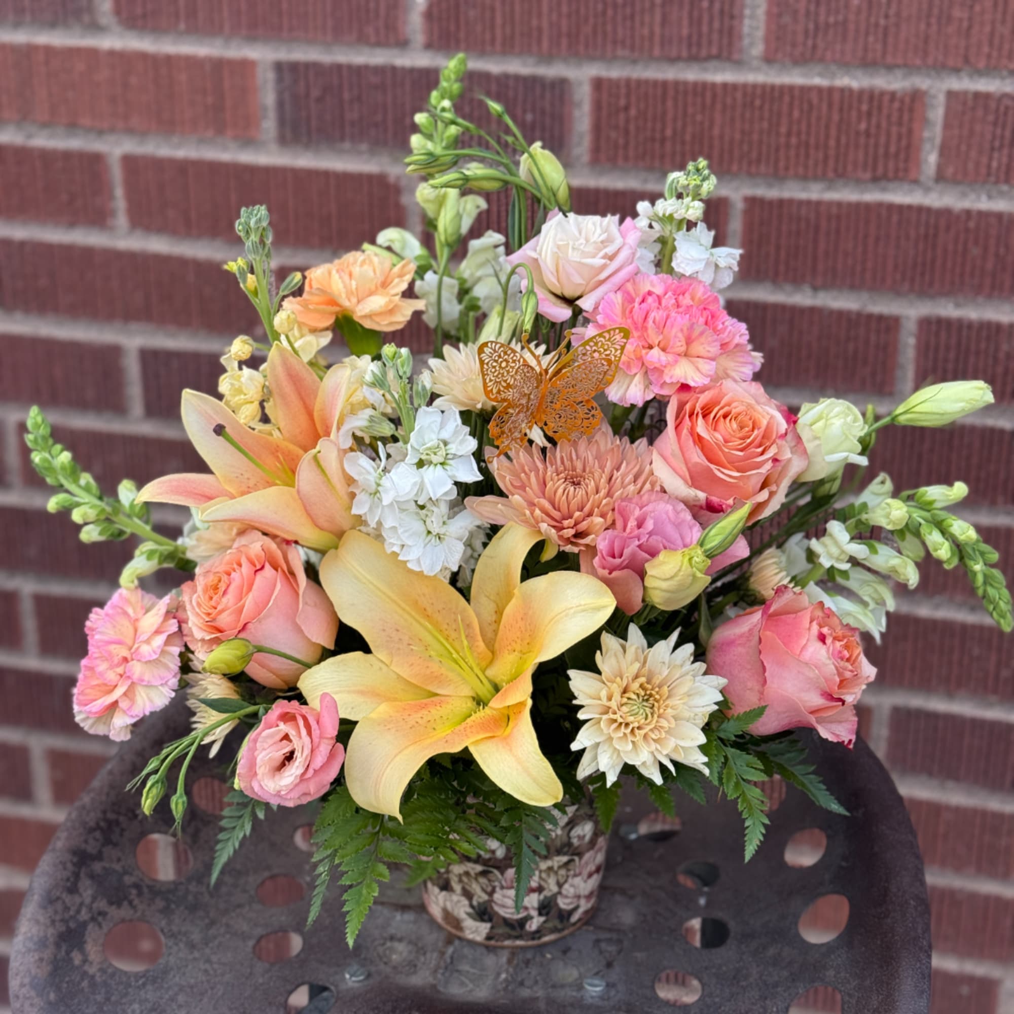 Mixed bouquet with pink roses, lilies, carnations, and white blooms in a patterned vase