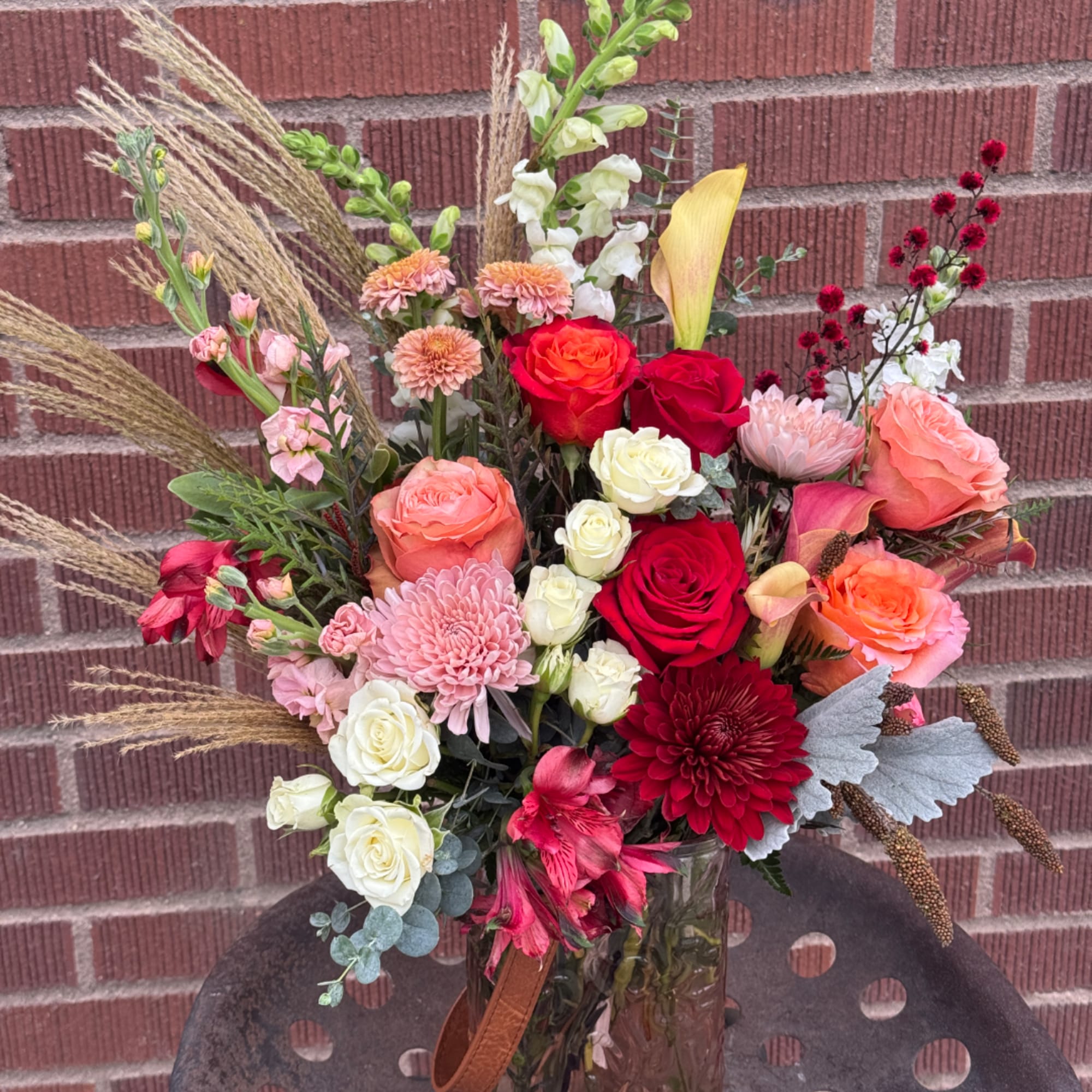 Mixed bouquet of roses, calla lilies, and chrysanthemums in a glass vase