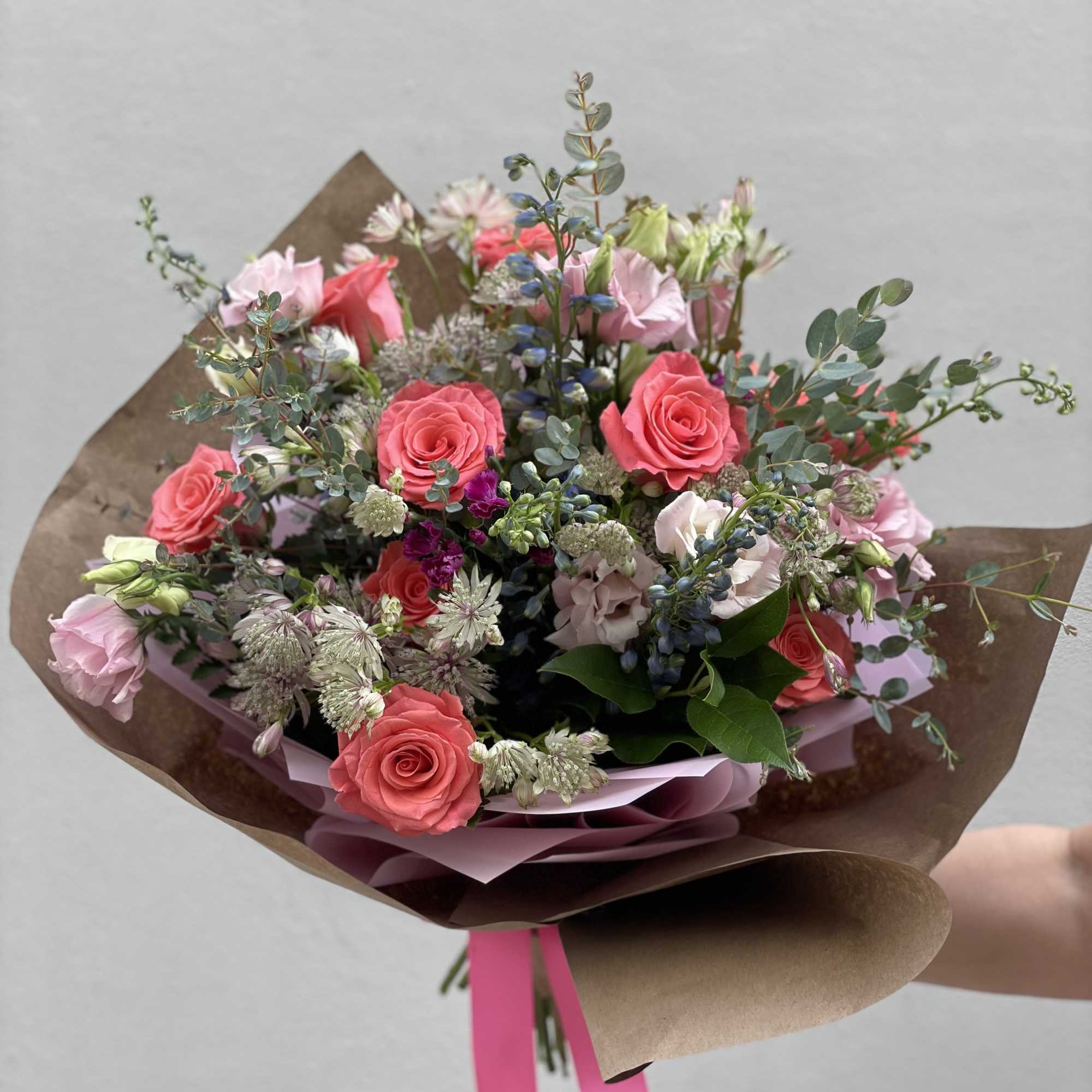 Hand-tied bouquet of pink roses and pale blooms wrapped in brown paper
