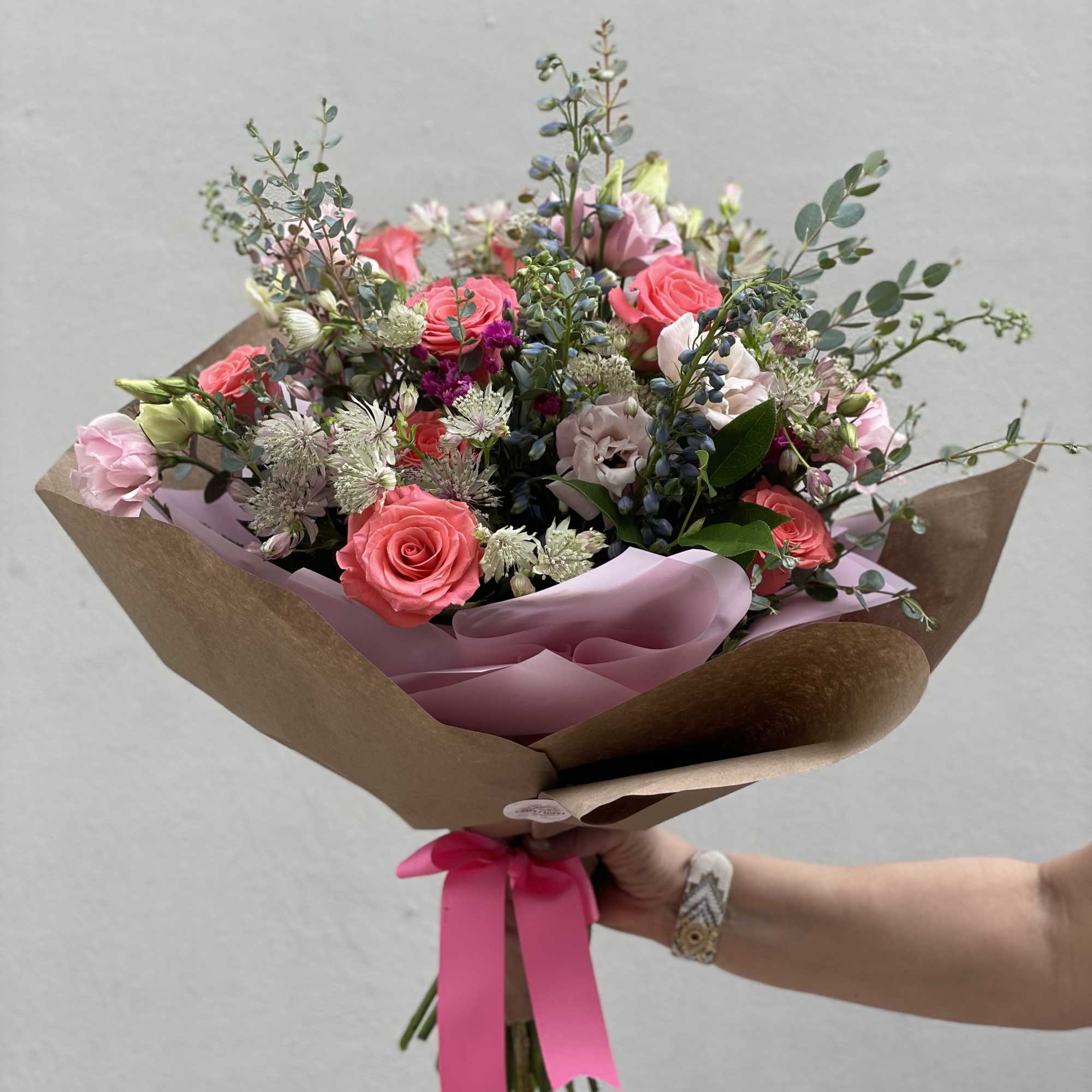 Hand-tied bouquet of pink roses and mixed blooms wrapped in brown paper