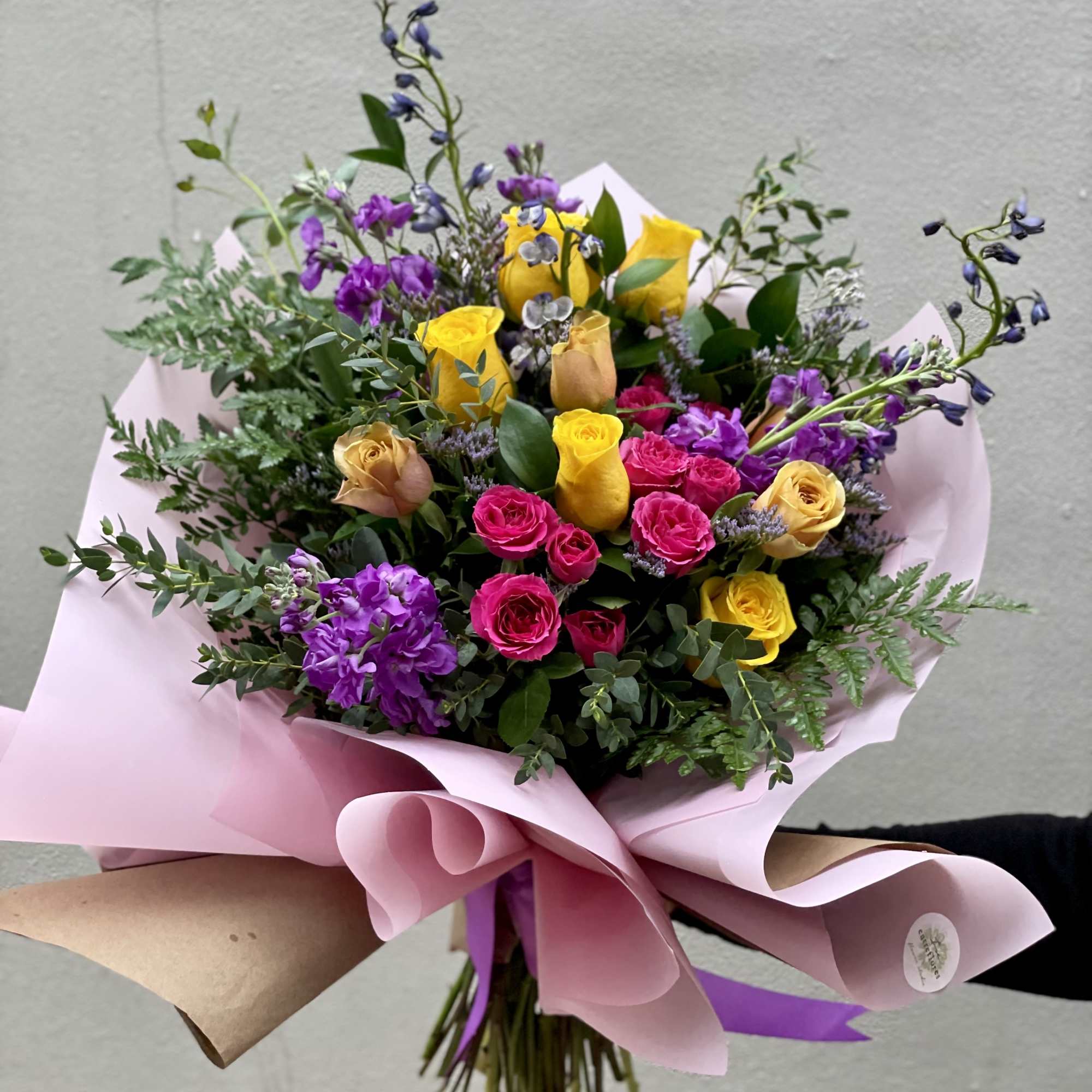Bouquet of yellow, pink, and purple roses wrapped in pink paper