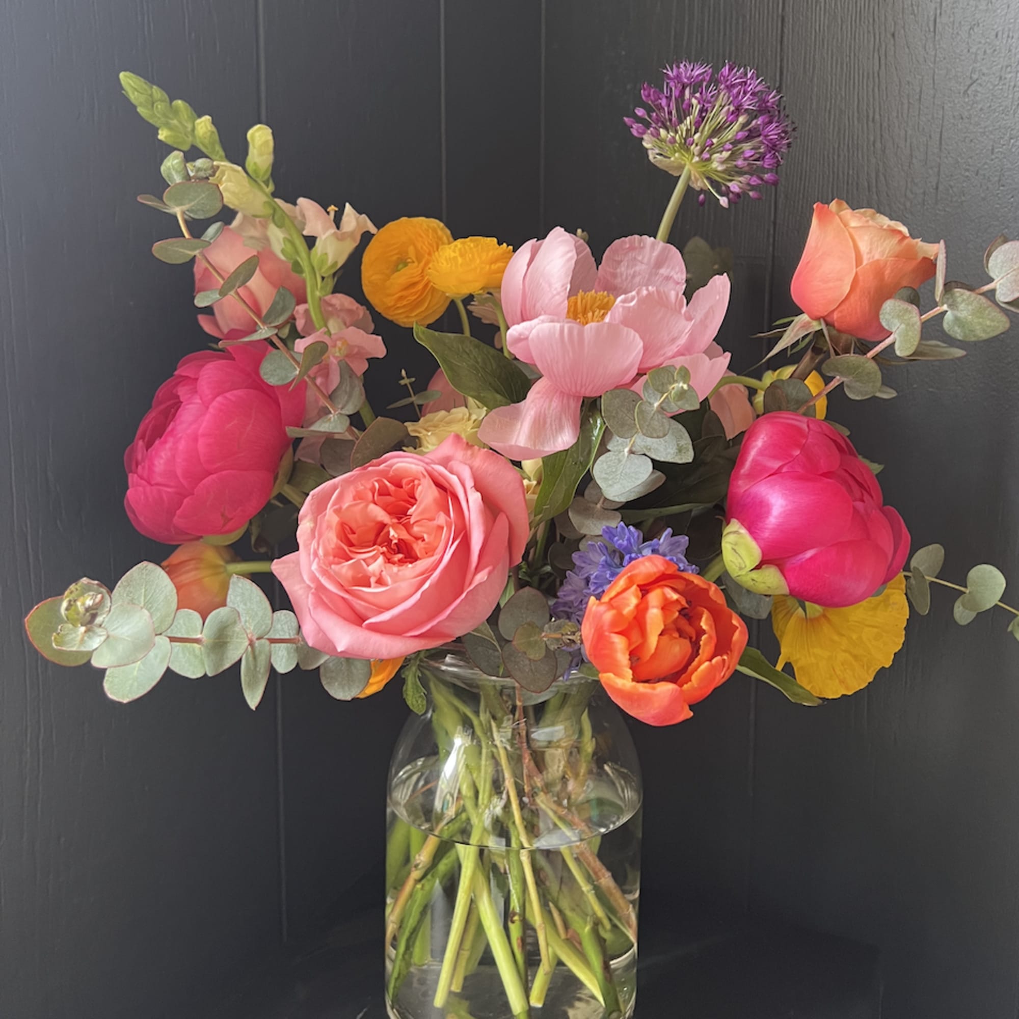 Colorful mixed bouquet in a clear glass vase with pink, orange, and yellow blooms
