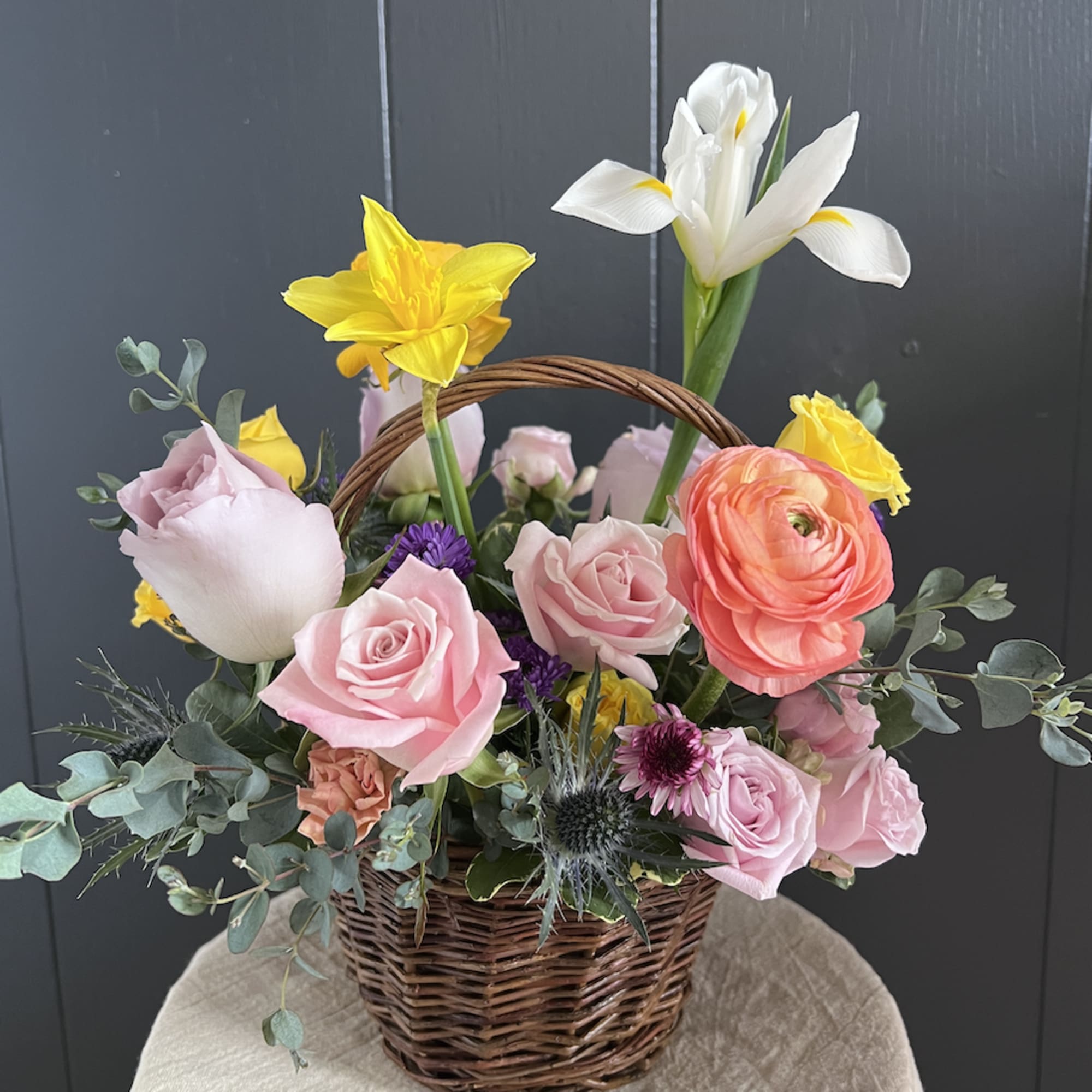 Basket arrangement with pink roses, yellow daffodils, and white iris
