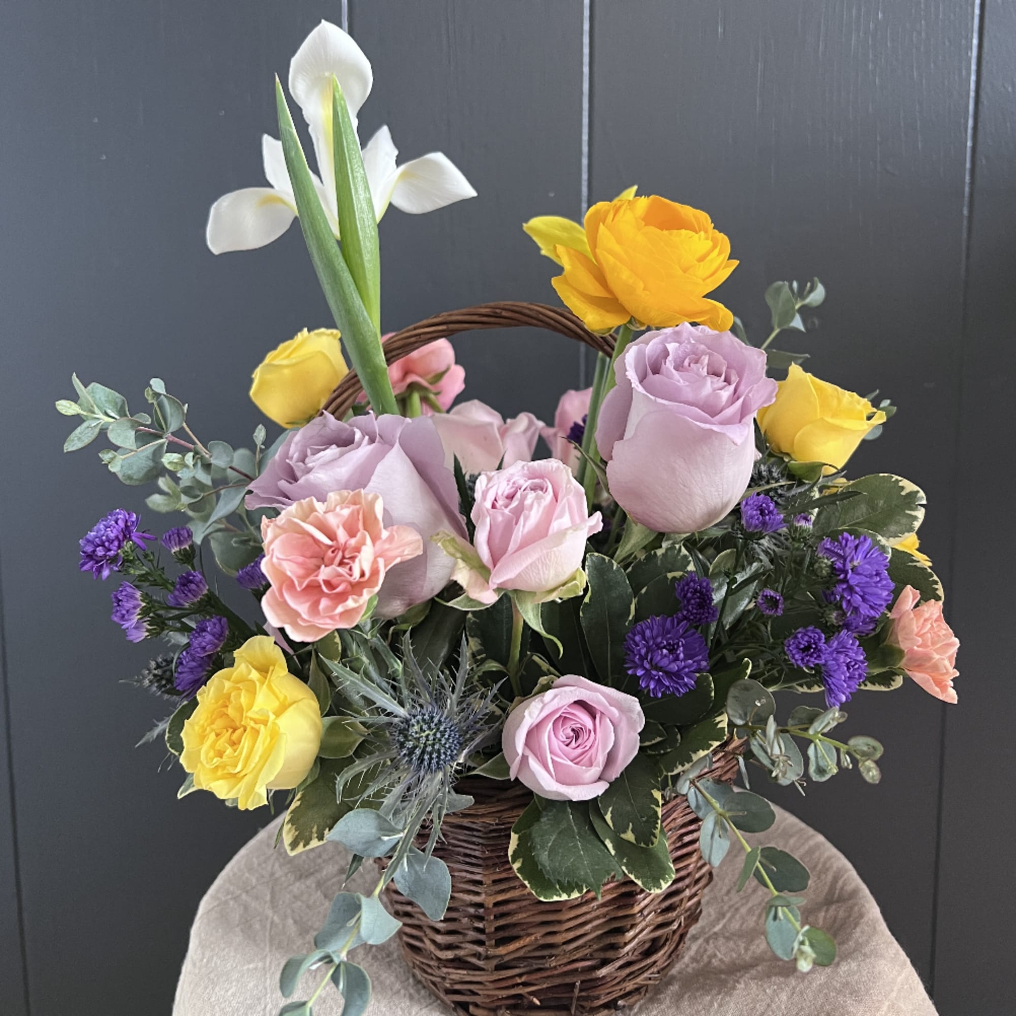 Mixed bouquet in a wicker basket with roses, calla lilies, and purple flowers